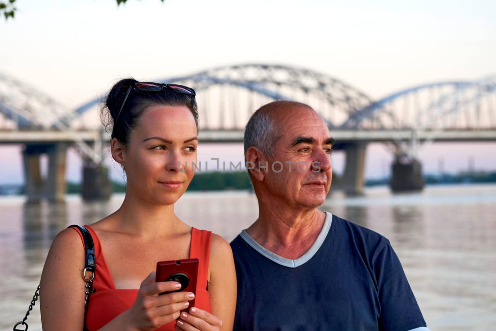 Positive pleased young woman and elderly man on the evening river bank, bridge by jovani68