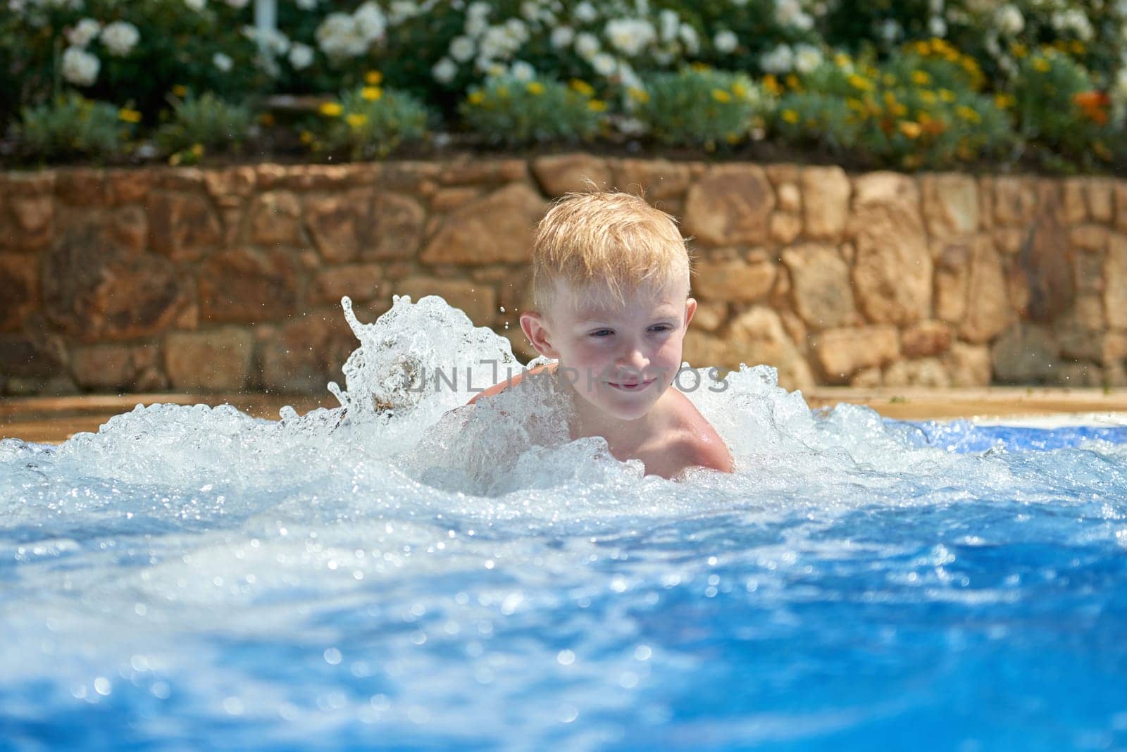 Young boy kid child eight years old splashing in swimming pool having fun leisure activity. Boy happy swimming in a pool. Activities on the pool, children swimming and playing in water, happiness and summertime