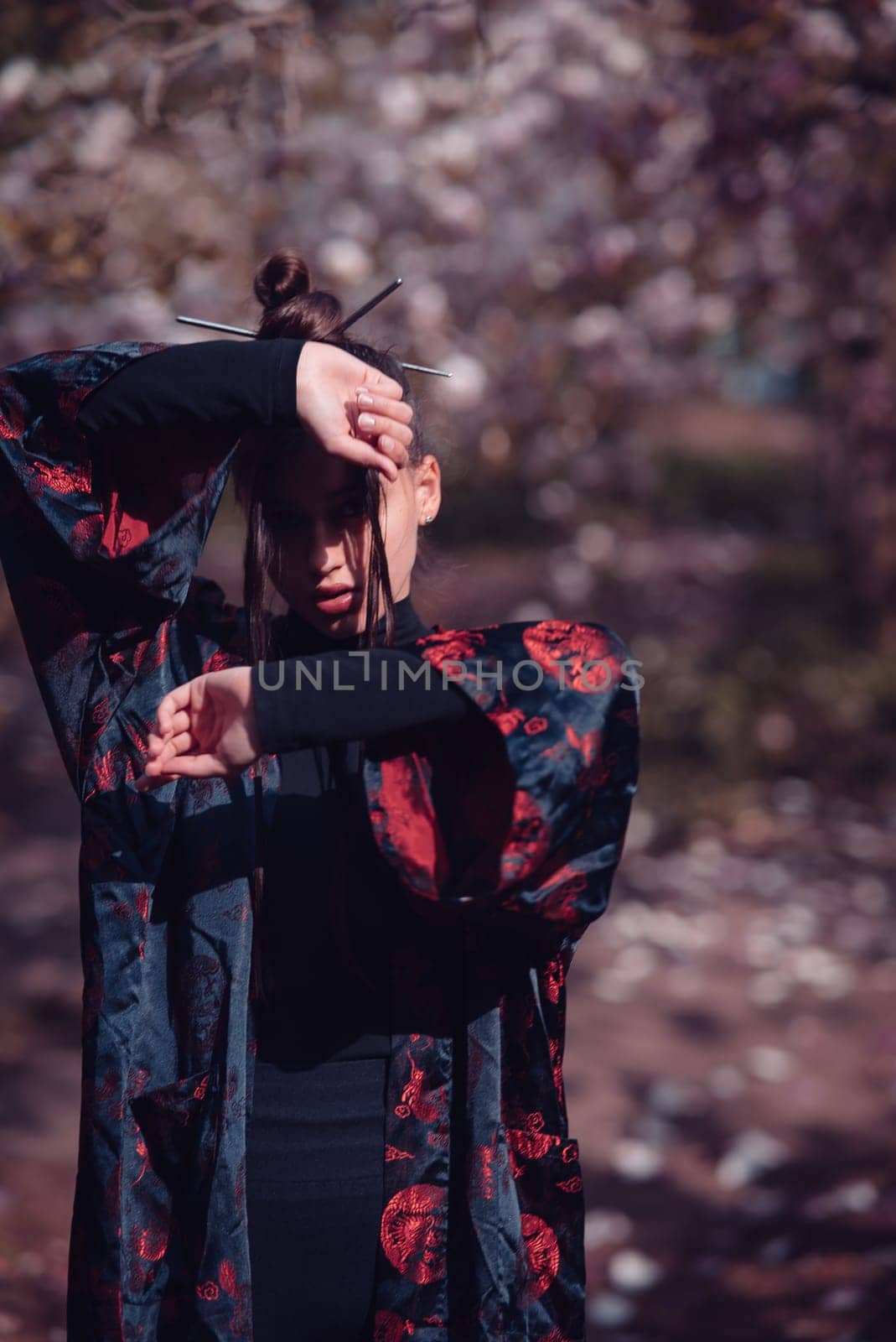 Beautiful dramatic young woman wearing kimono raising her hands to hide her face with cherry blossoms, sakura view. High quality photo