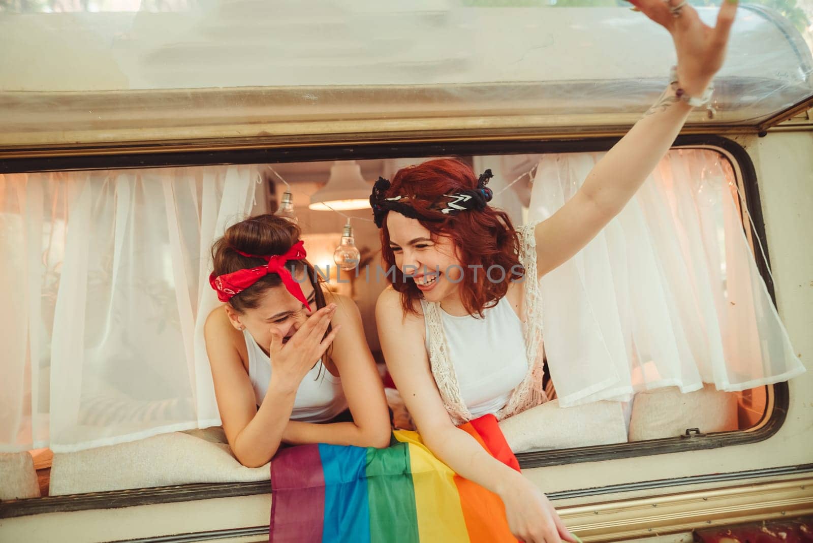 Portrait of a cute lesbian couple. Two girls spend time tenderly together watching movie on laptop in a camper trailer with LGBT flag on the wall. Love and attitude. LGBT concept. High quality photo