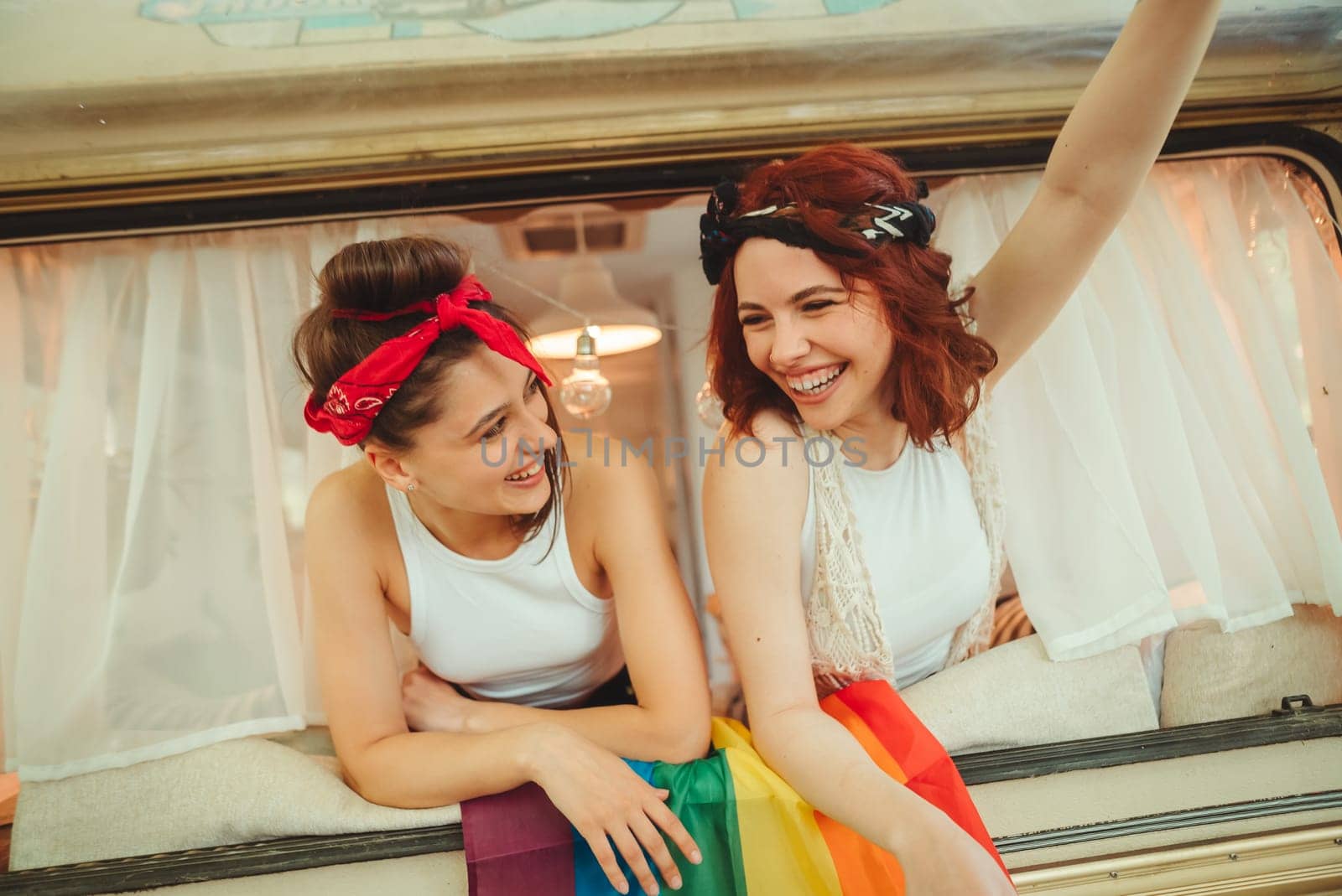 Portrait of a cute lesbian couple. Two girls spend time tenderly together watching movie on laptop in a camper trailer with LGBT flag on the wall. Love and attitude. LGBT concept. High quality photo