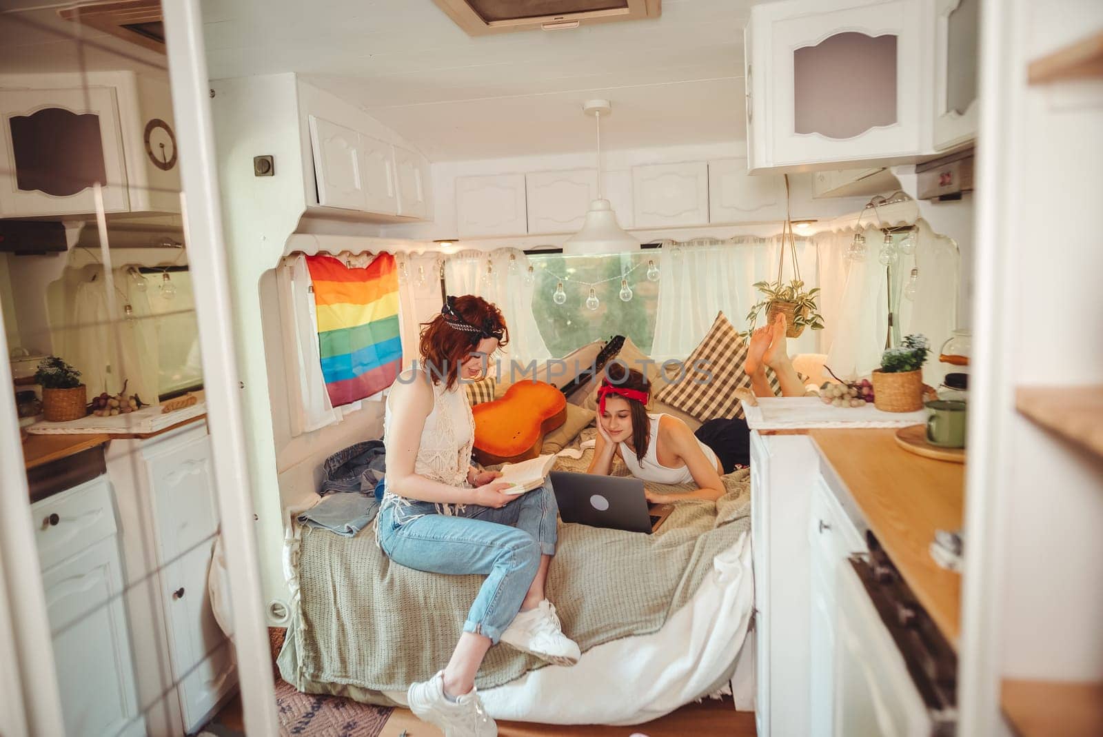 Portrait of a cute lesbian couple. Two girls spend time tenderly together watching movie on laptop in a camper trailer with LGBT flag on the wall. Love and attitude. LGBT concept. High quality photo