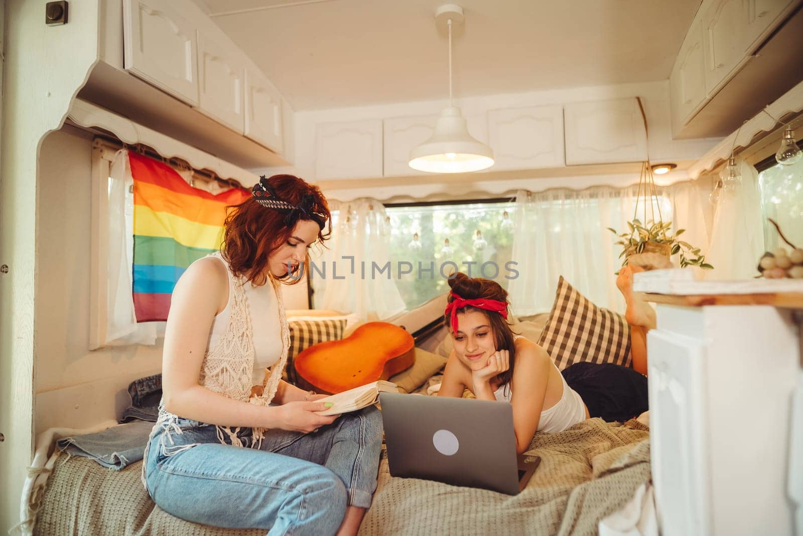 Portrait of a cute lesbian couple. Two girls spend time tenderly together watching movie on laptop in a camper trailer with LGBT flag on the wall. Love and attitude. LGBT concept. High quality photo