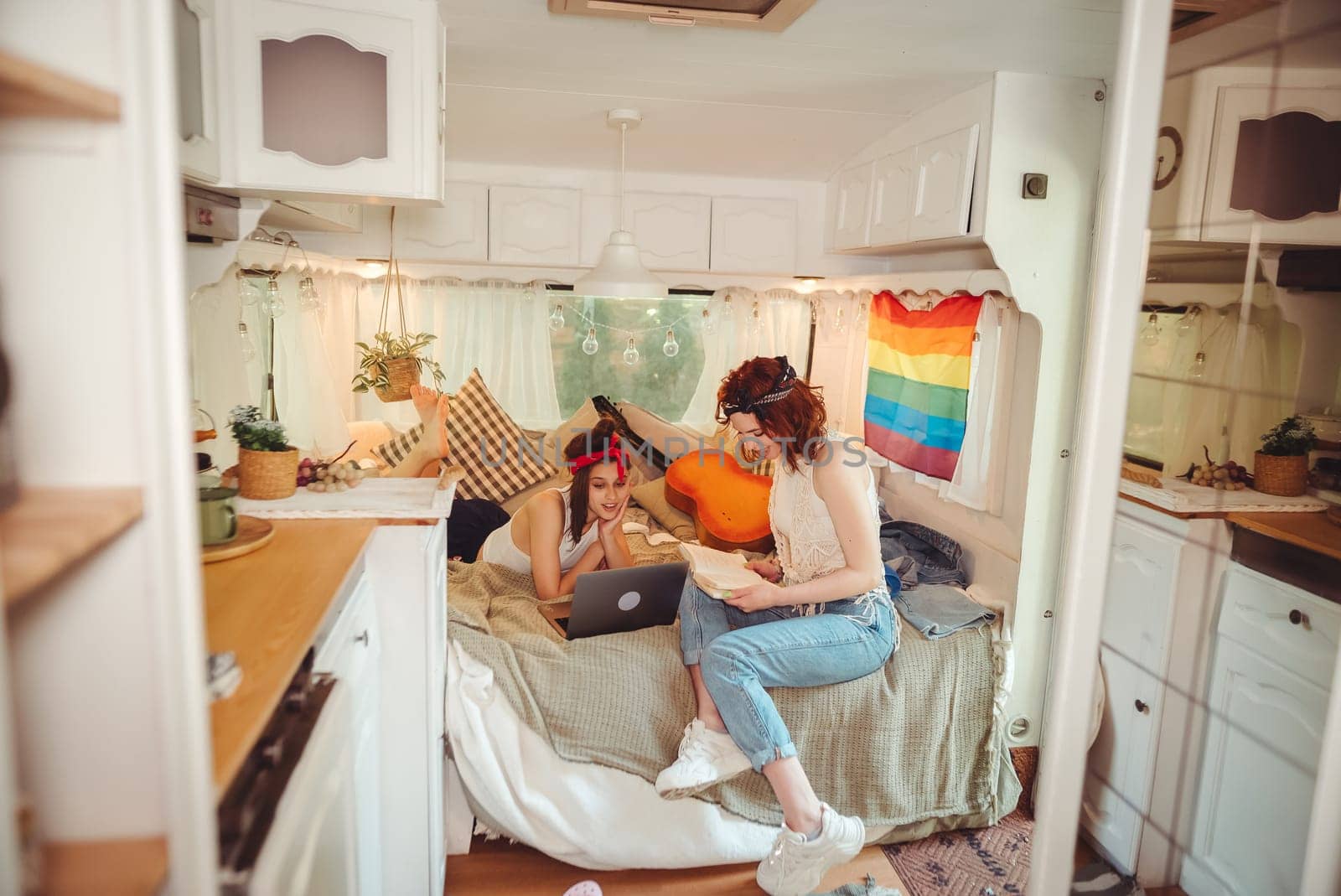 Portrait of a cute lesbian couple. Two girls spend time tenderly together watching movie on laptop in a camper trailer with LGBT flag on the wall. Love and attitude. LGBT concept. High quality photo