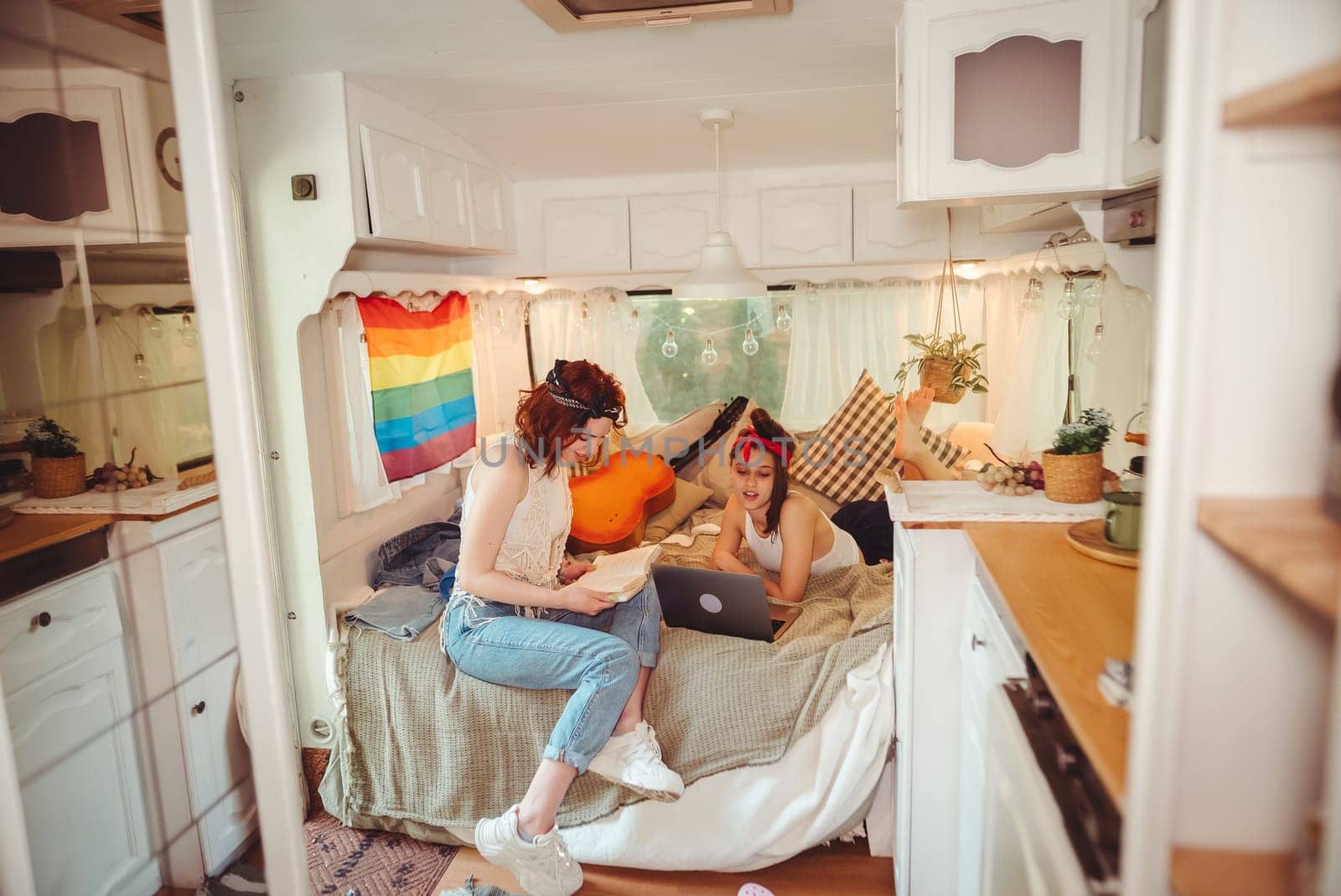 Portrait of a cute lesbian couple. Two girls spend time tenderly together watching movie on laptop in a camper trailer with LGBT flag on the wall. Love and attitude. LGBT concept. High quality photo