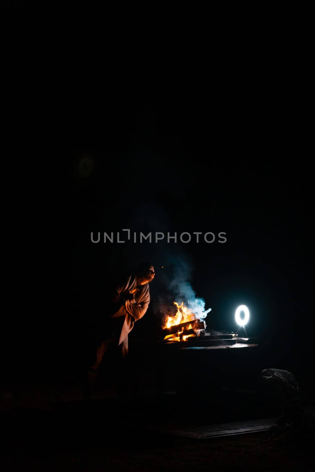 Man preparing bbq grill to cook on fire. Outside dark shot. Freeze moment of fire. High quality photo