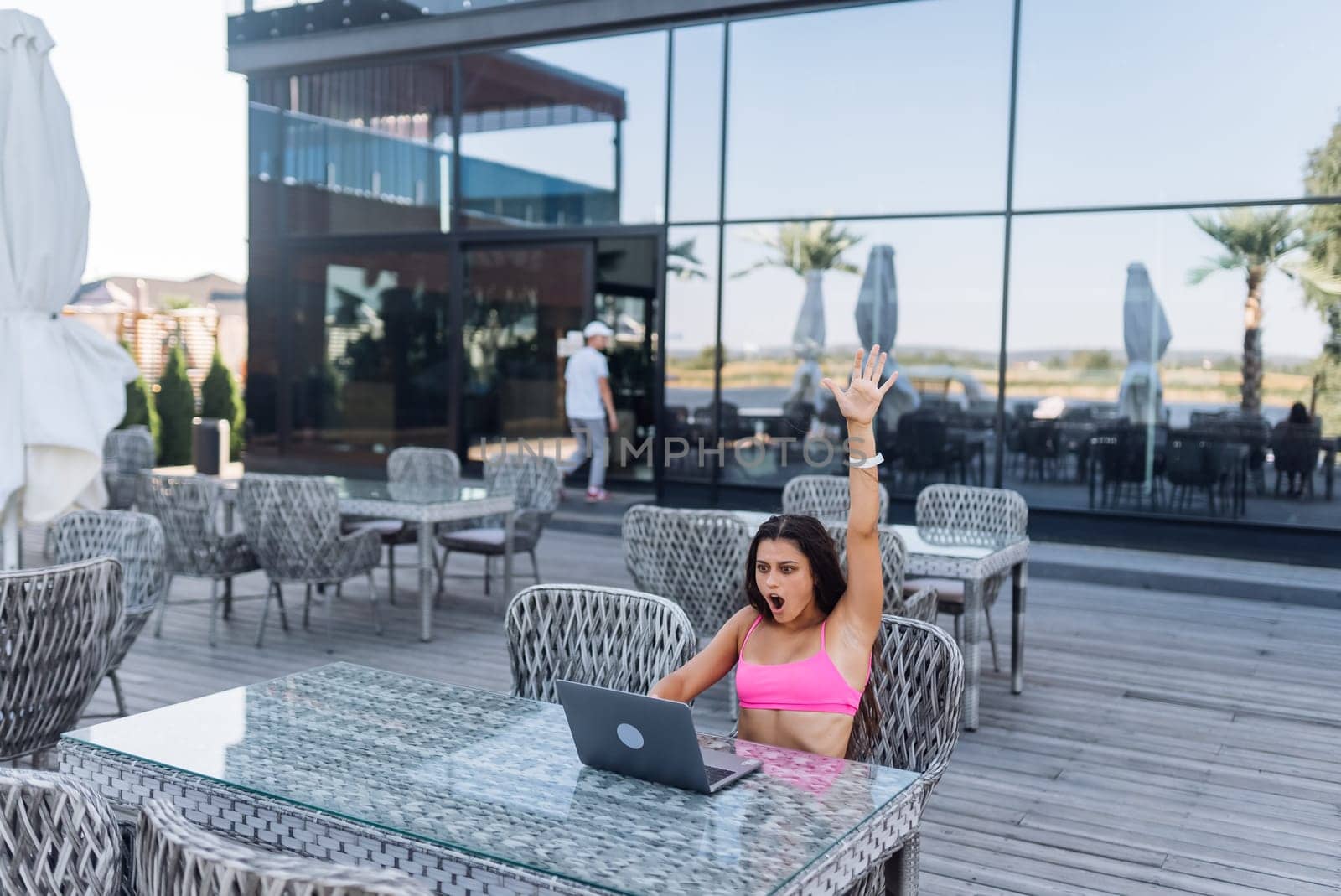 Cute young woman with crazy emotions sitting on terrace, while using laptop for work at summer day