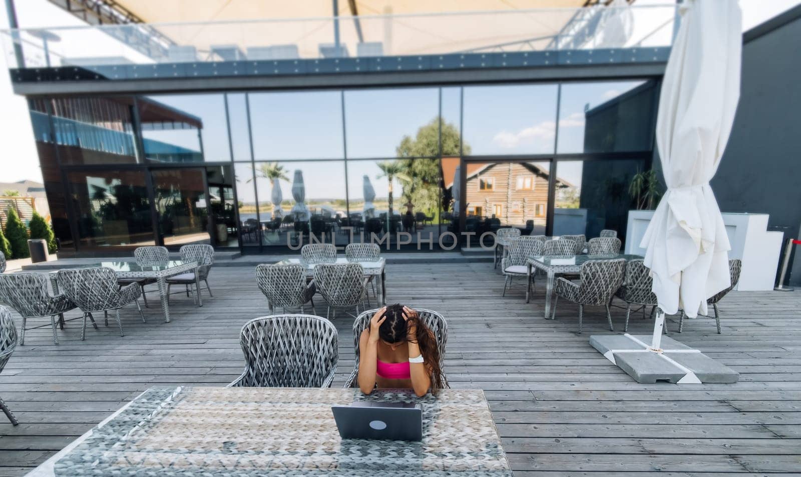 Cute young woman sitting on terrace, while using laptop for work at summer day