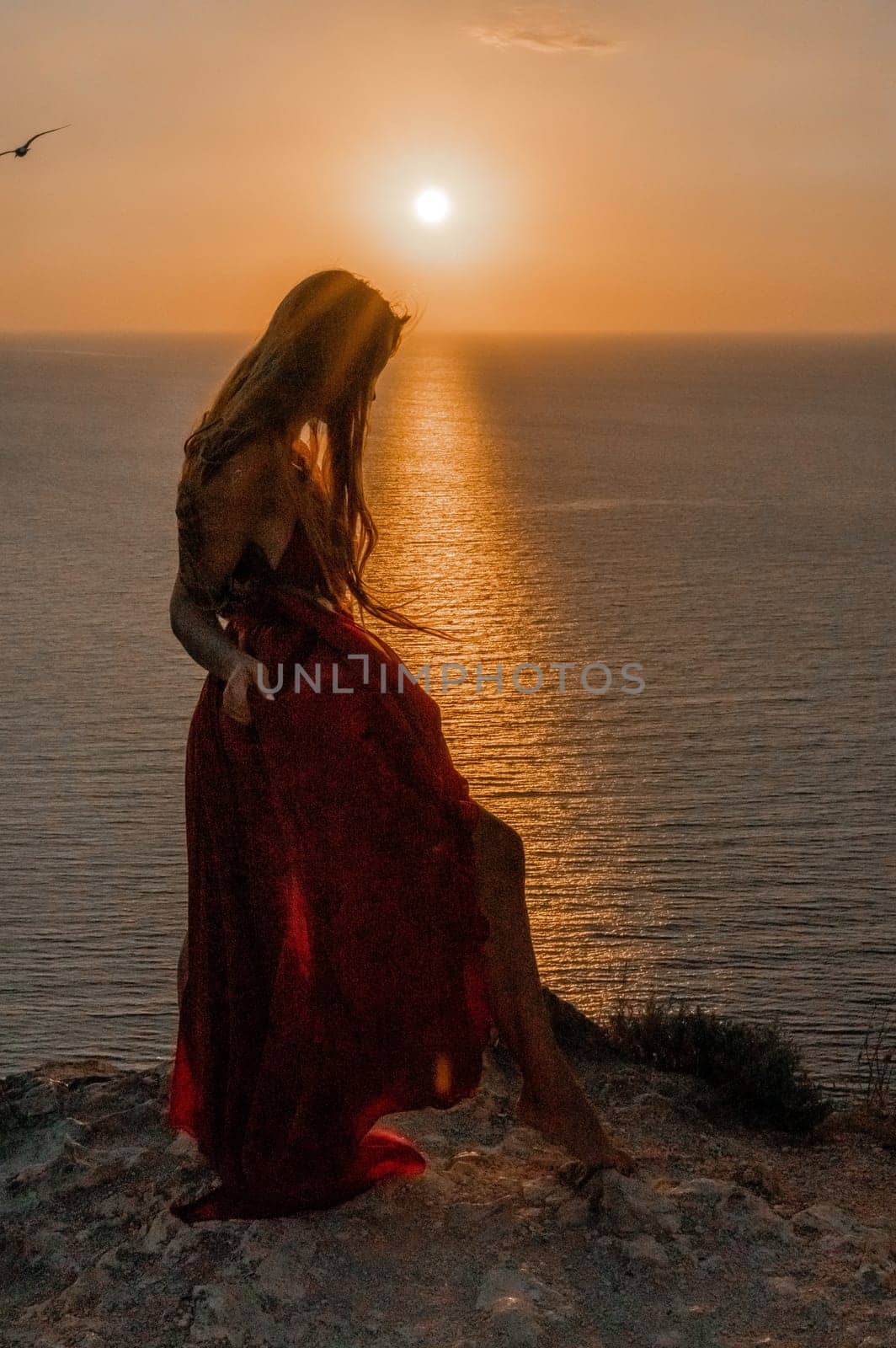 Woman sunset sea red dress, back view a happy beautiful sensual woman in a red long dress posing on a rock high above the sea on sunset