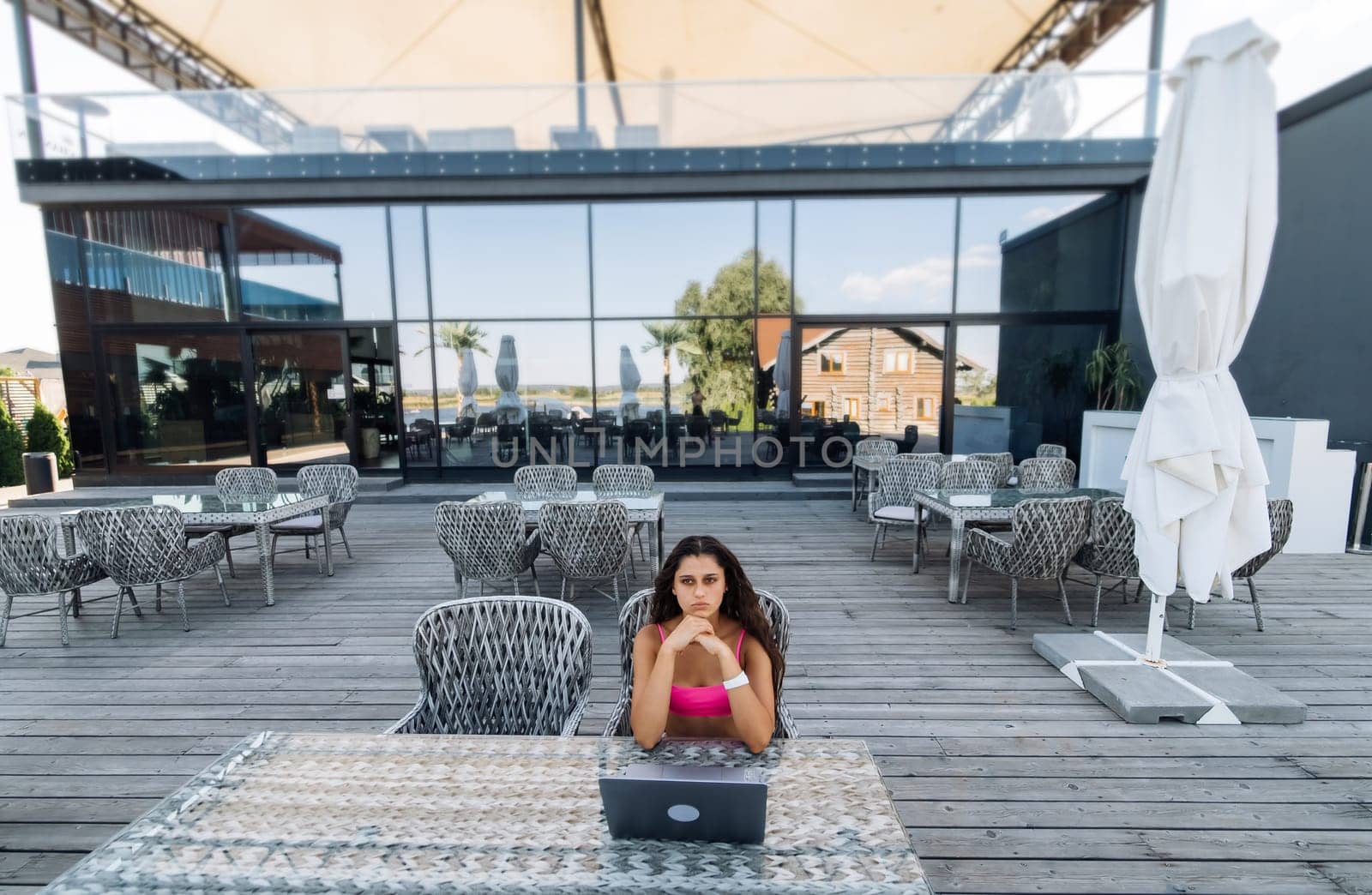 Cute young woman sitting on terrace, while using laptop for work at summer day
