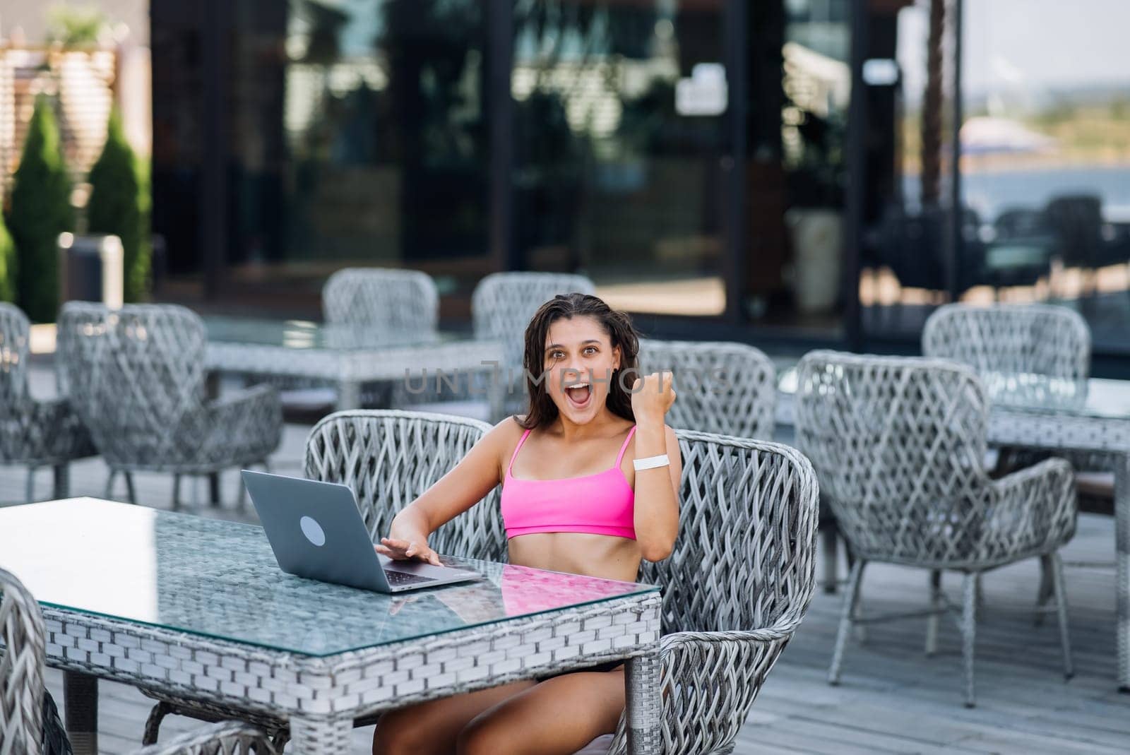Cute young woman sitting on terrace, happy with hands up winner at summer day