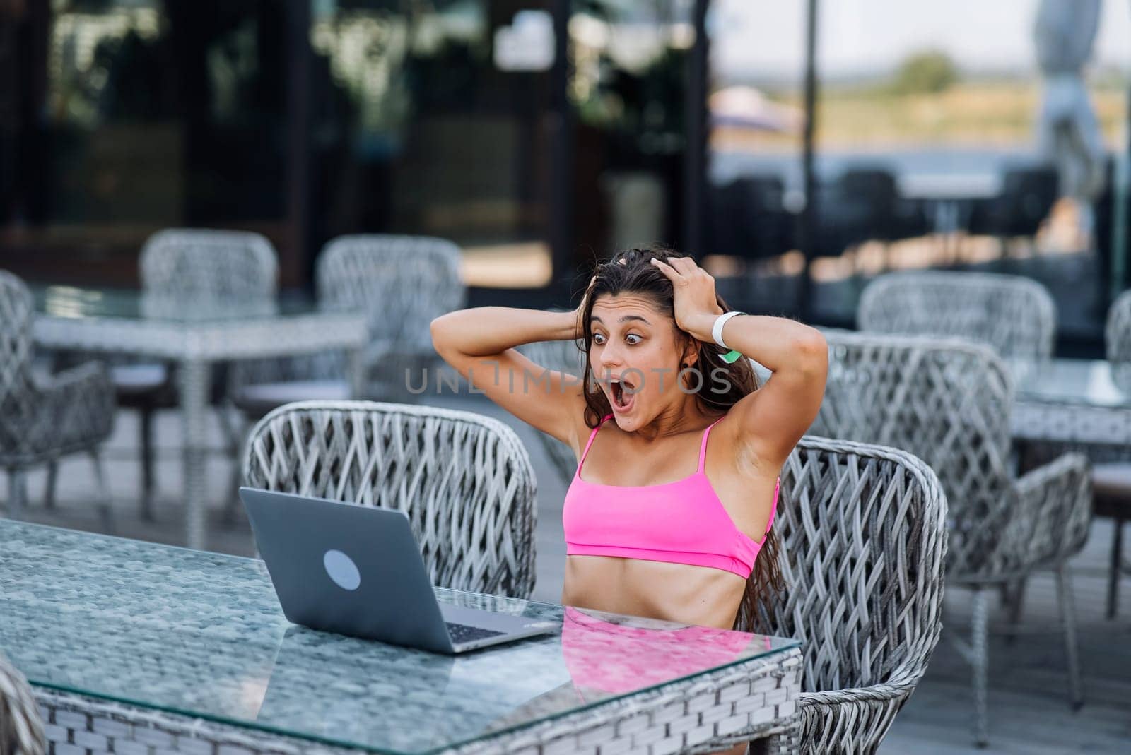 Cute young woman sitting on terrace, while using laptop for work at summer day
