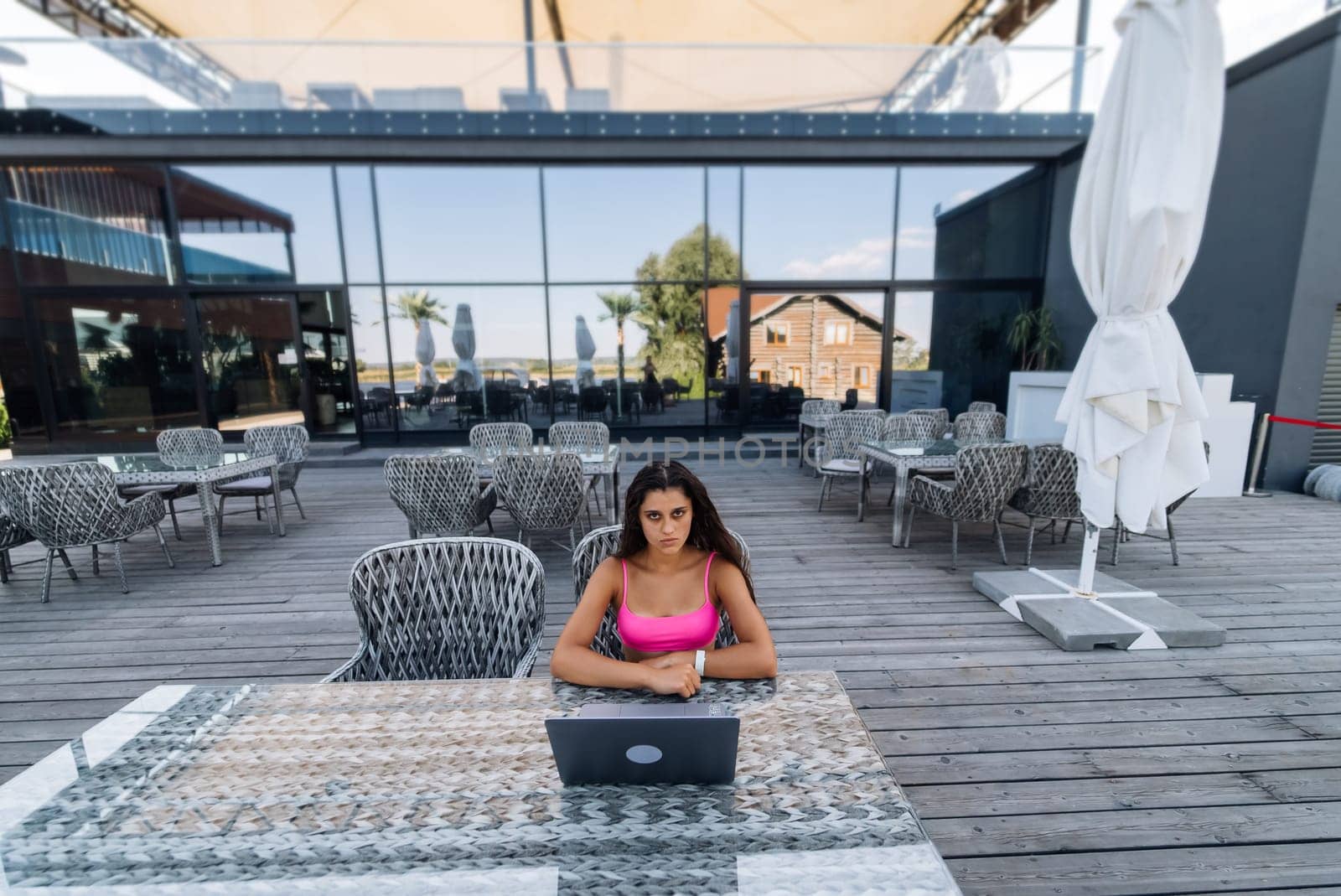 Cute young woman in swimsuit working on laptop sitting on terrace on the beach by teksomolika