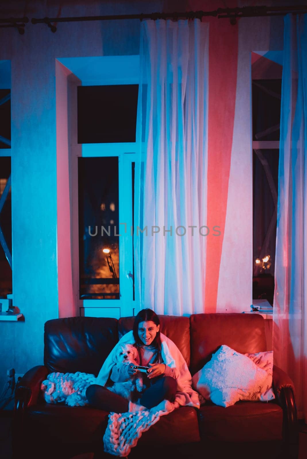 Beautiful young girl watching movie at home in a dark room with a popcorn bucket and playing with her dog and sits in front of a monitor or TV watching movie. Crazy emotions. High quality photo