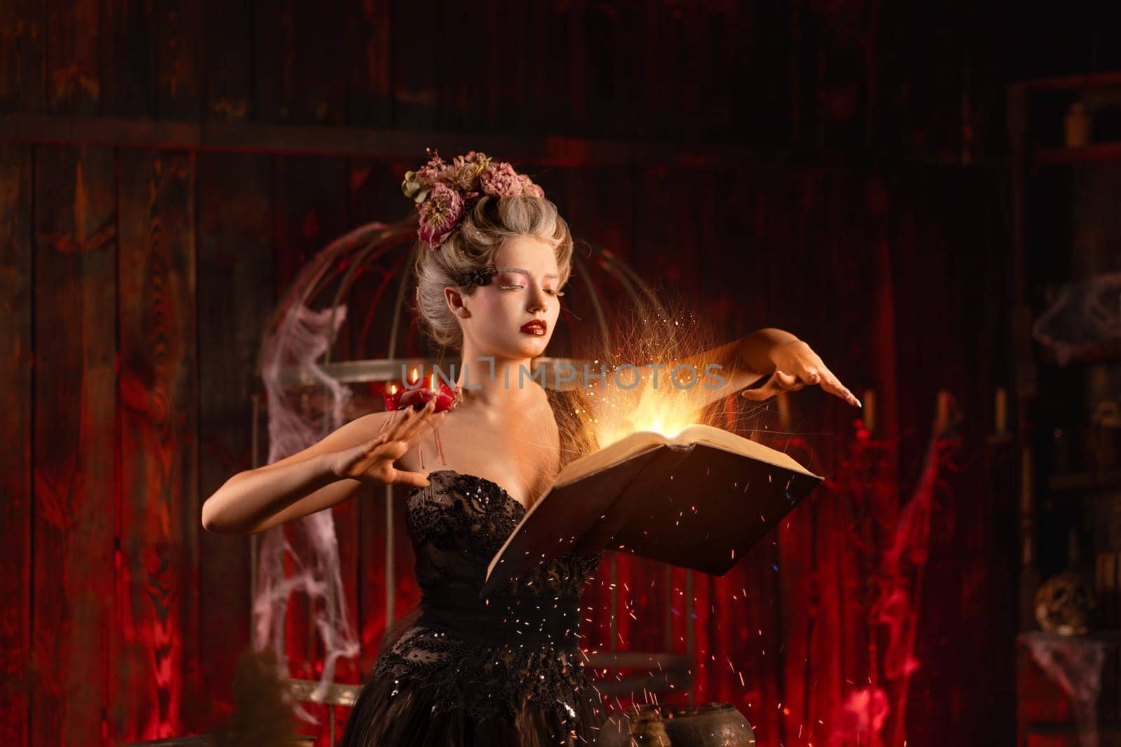 Charming woman witch flowers in hair vintage black dress with book of spell in the old castle. Halloween. Celebration. Witchcraft concept, fairy tale mystic atmosphere. Conjure magic spells