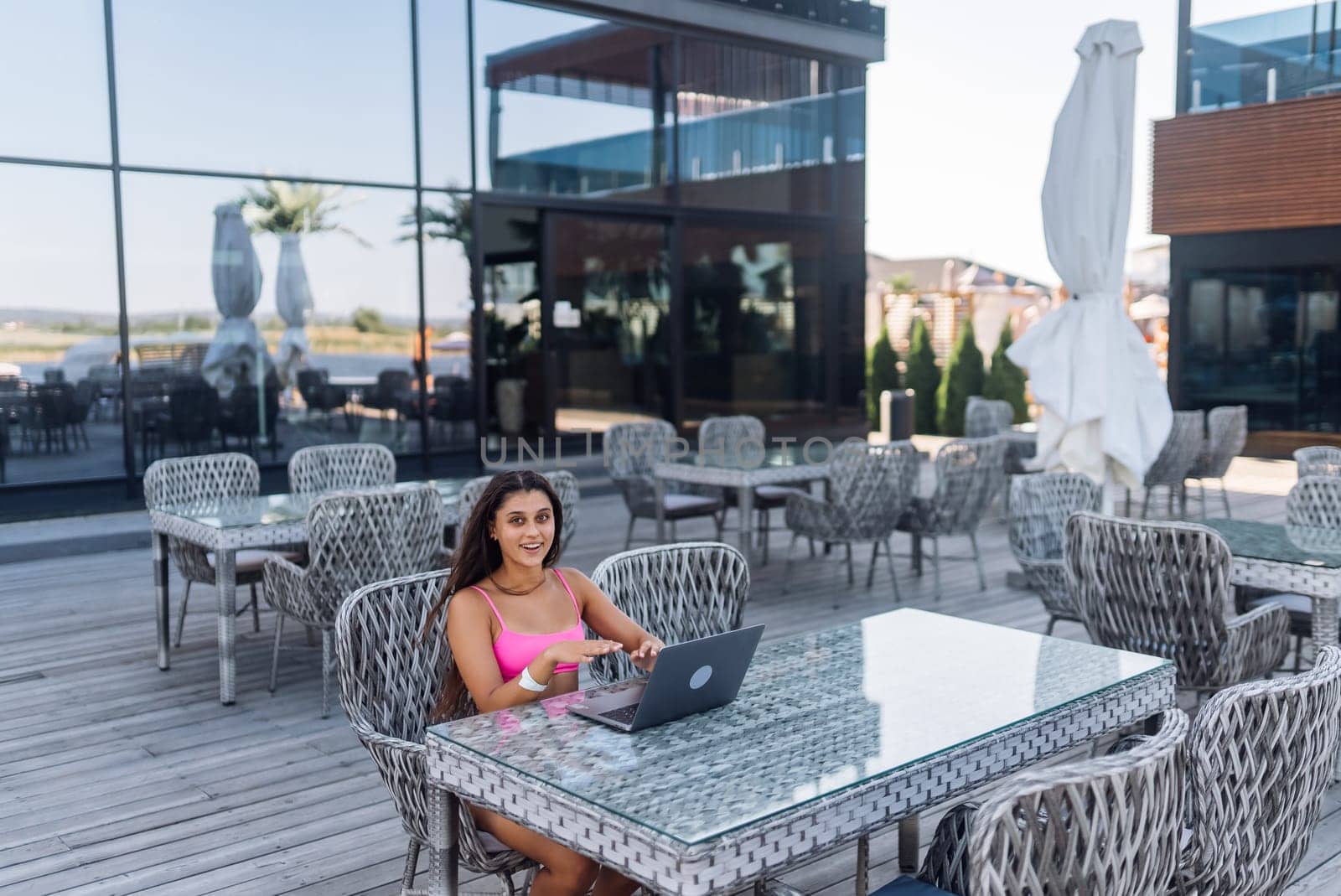 Cute young woman in swimsuit working on laptop sitting on terrace on the beach by teksomolika
