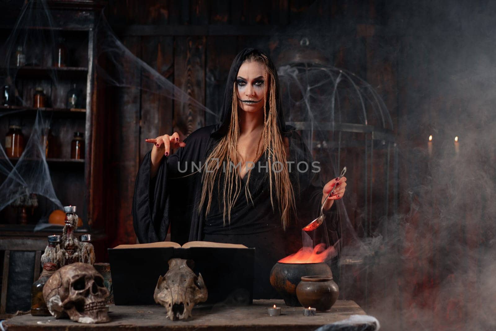 Halloween, witch use magic book and cauldron prepare poison or love potion. Black magic female wizard in dark room cage spider web human skull. Necromancer cooking magic potion. voodoo magic