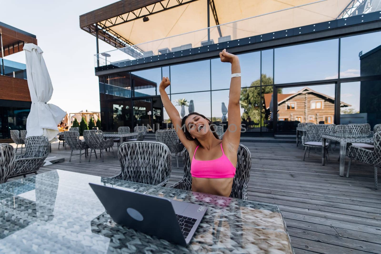 Cute young woman with crazy emotions sitting on terrace, while using laptop for work at summer day