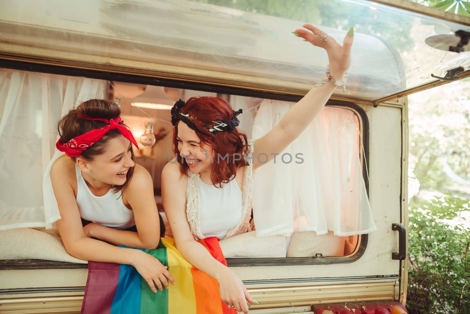 Portrait of a cute lesbian couple. Two girls spend time tenderly together watching movie on laptop in a camper trailer with LGBT flag on the wall. Love and attitude. LGBT concept. High quality photo