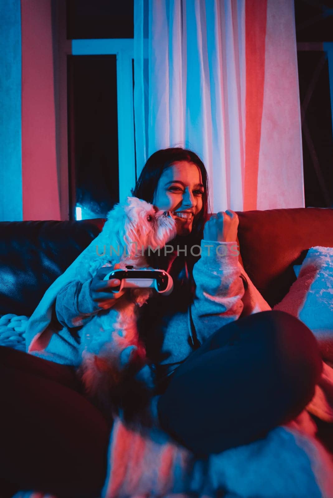 A gamer or a streamer girl at home in a dark room with a game controller playing with her dog and sits in front of a monitor or TV. High quality photo