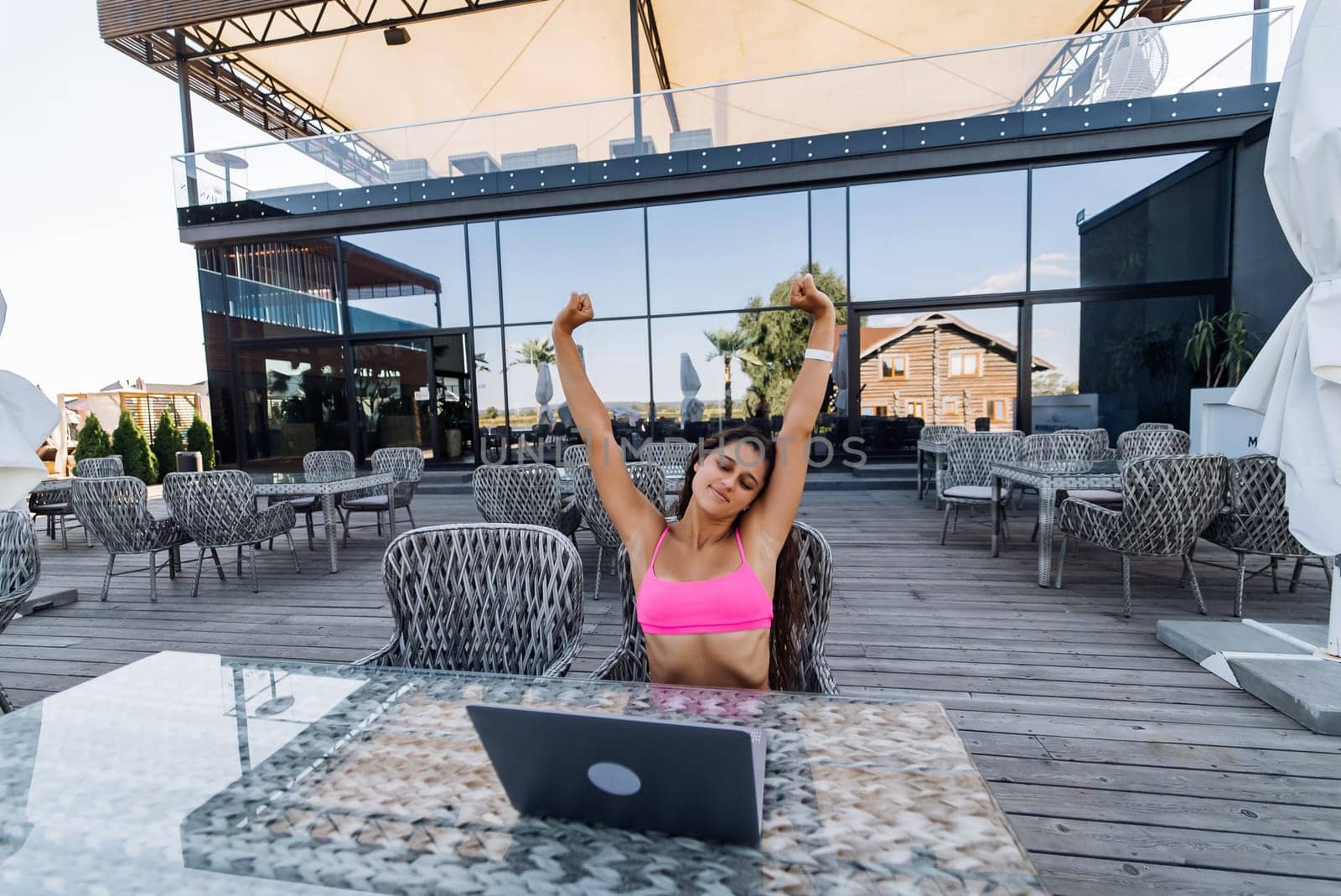 Cute young woman with crazy emotions sitting on terrace, while using laptop for work at summer day