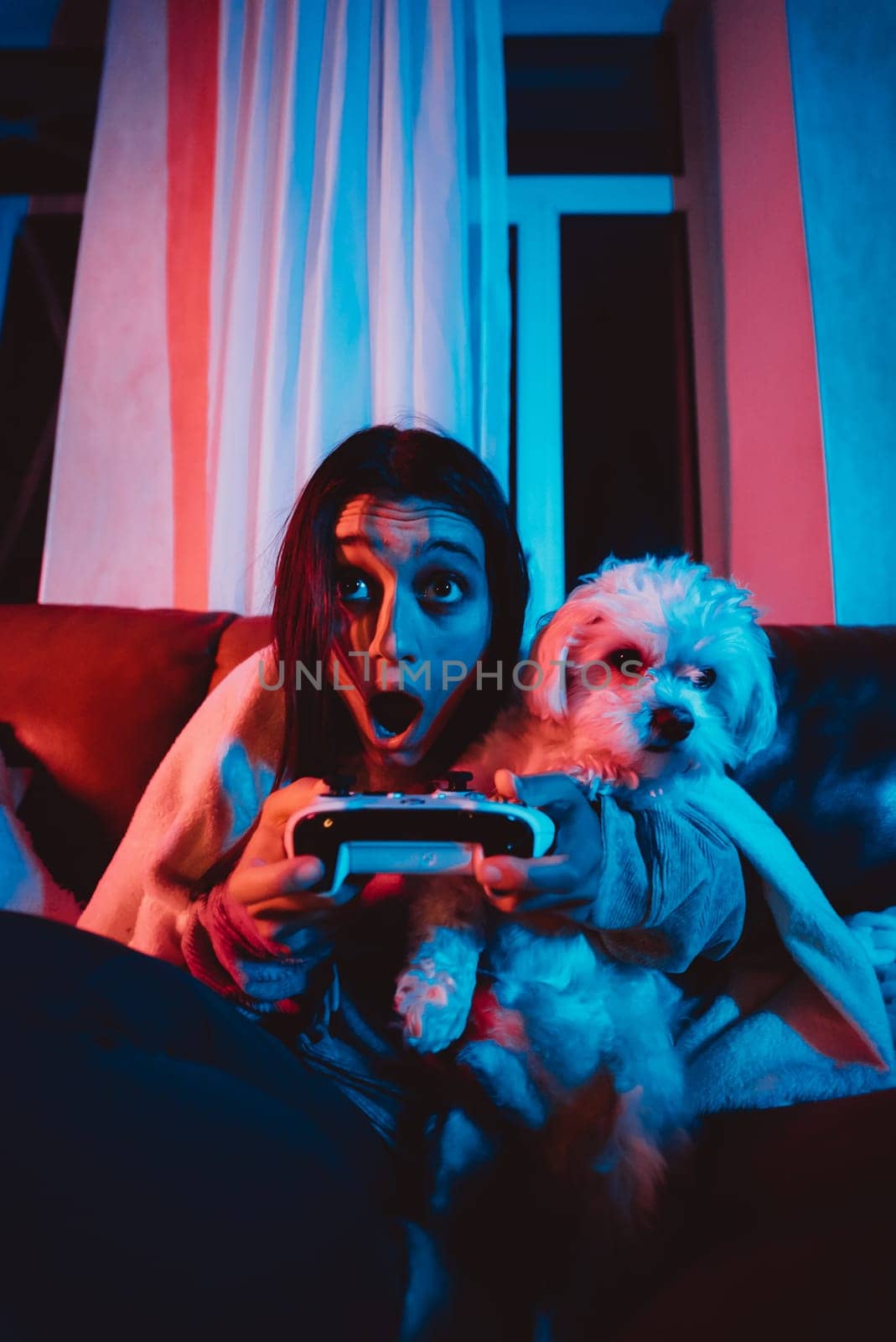 Close up portrait of A gamer or a streamer girl at home in a dark room with a game controller playing with her dog and sits in front of a monitor or TV. High quality photo