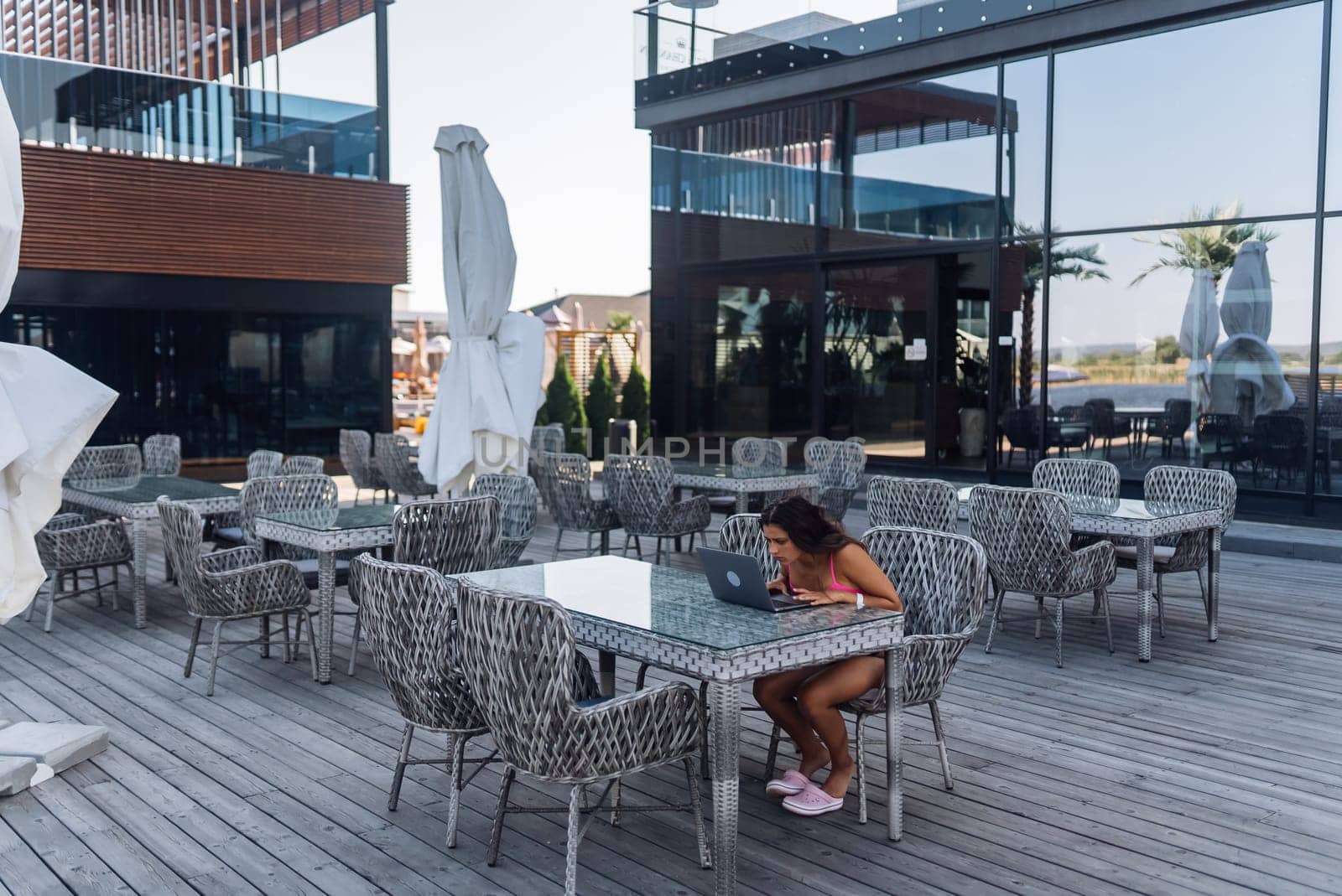 Cute young woman sitting on terrace, while using laptop for work at summer day