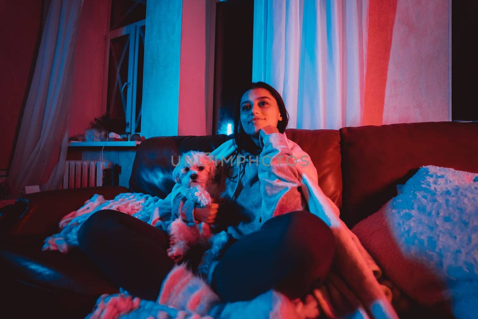 Close up portrait of A gamer or a streamer girl at home in a dark room with a game controller playing with her dog and sits in front of a monitor or TV. High quality photo