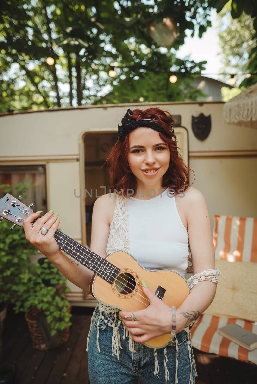 Happy hippie girl is having a good time with playing on guitar in camper trailer. Holiday, vacation, trip concept.High quality photo