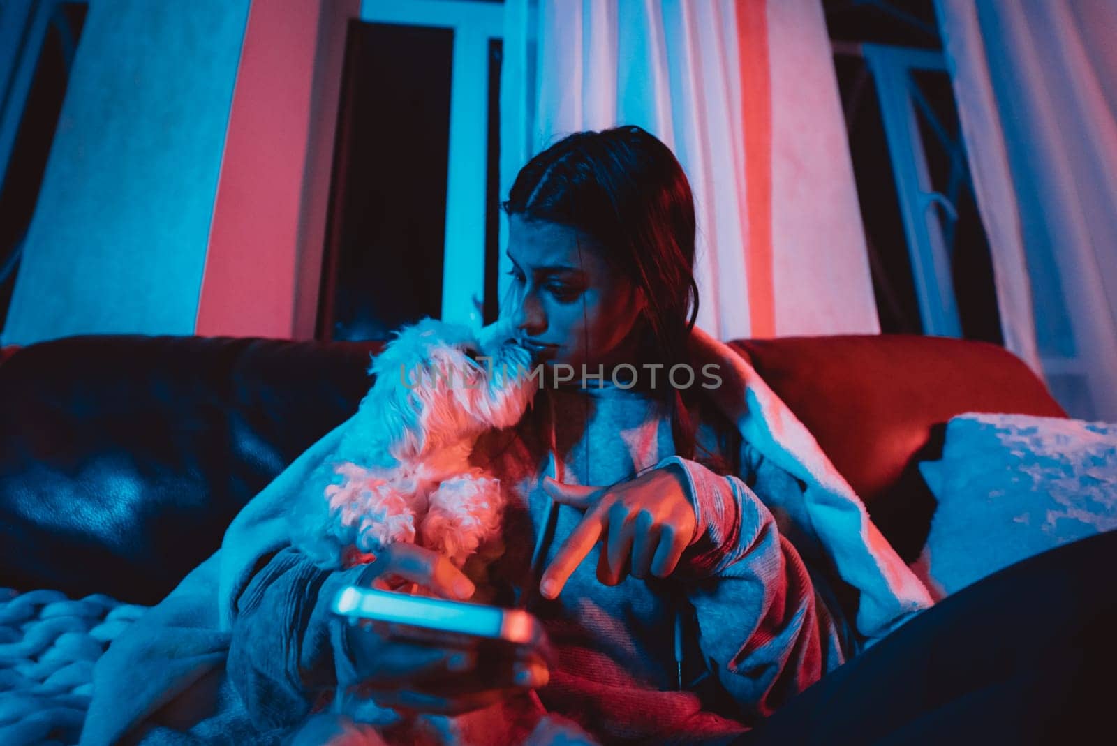 Beautiful young girl at home in a dark room playing with her dog and sits in front of a monitor or TV. High quality photo
