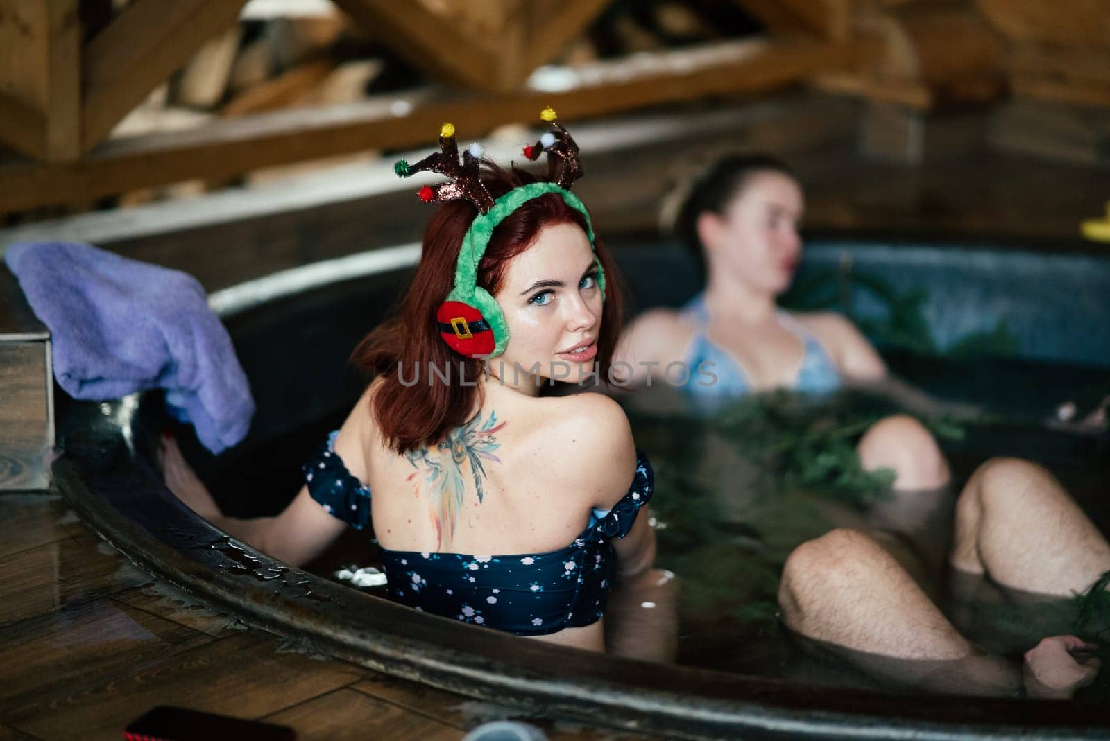 Young girls in bikinis bathing in an outdoor bathtub on winter holidays. Wooden cottage. High quality photo