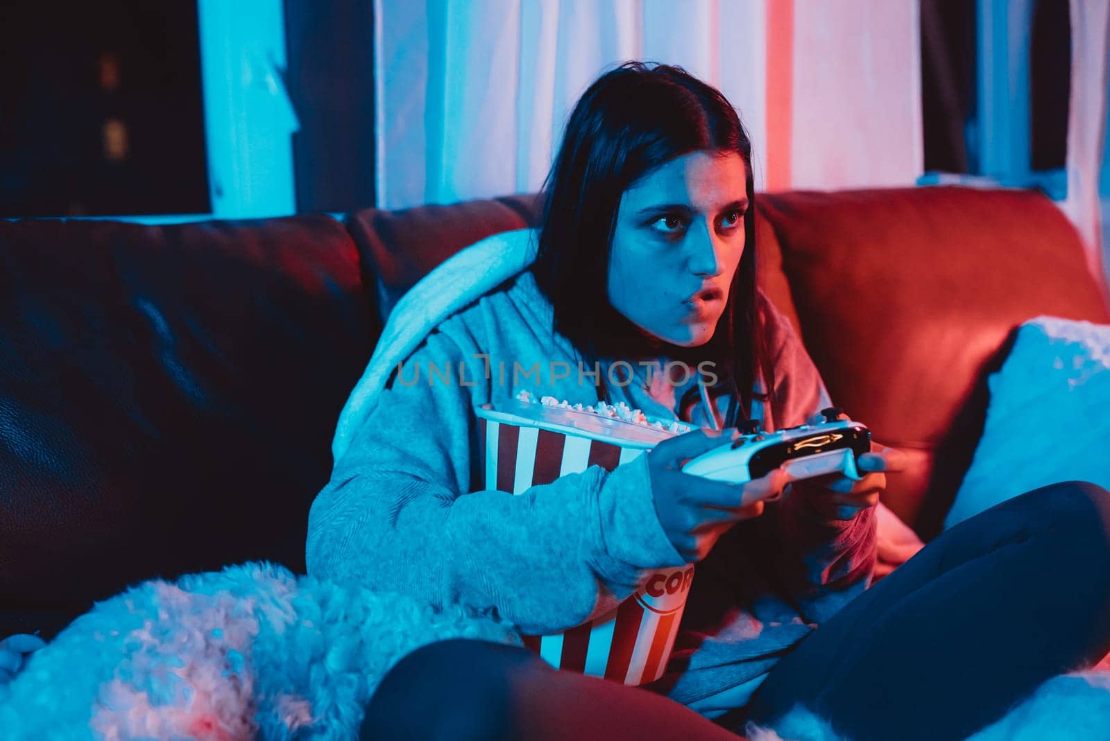 A gamer or a streamer girl at home in a dark room with a game controller and popcorn bucket playing with her dog and sits in front of a monitor or TV. High quality photo