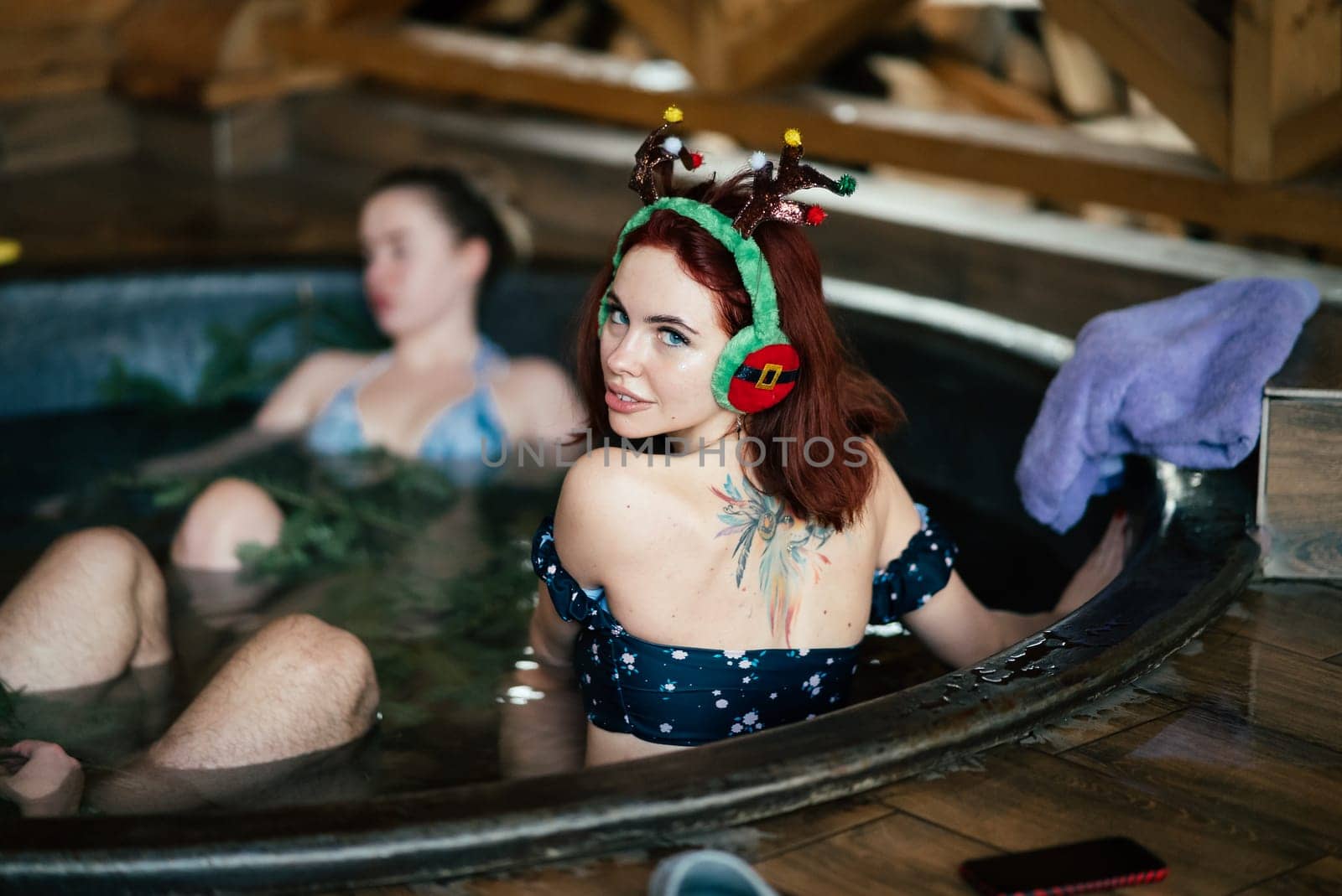 Young girls in bikinis bathing in an outdoor bathtub on winter holidays. Wooden cottage. High quality photo