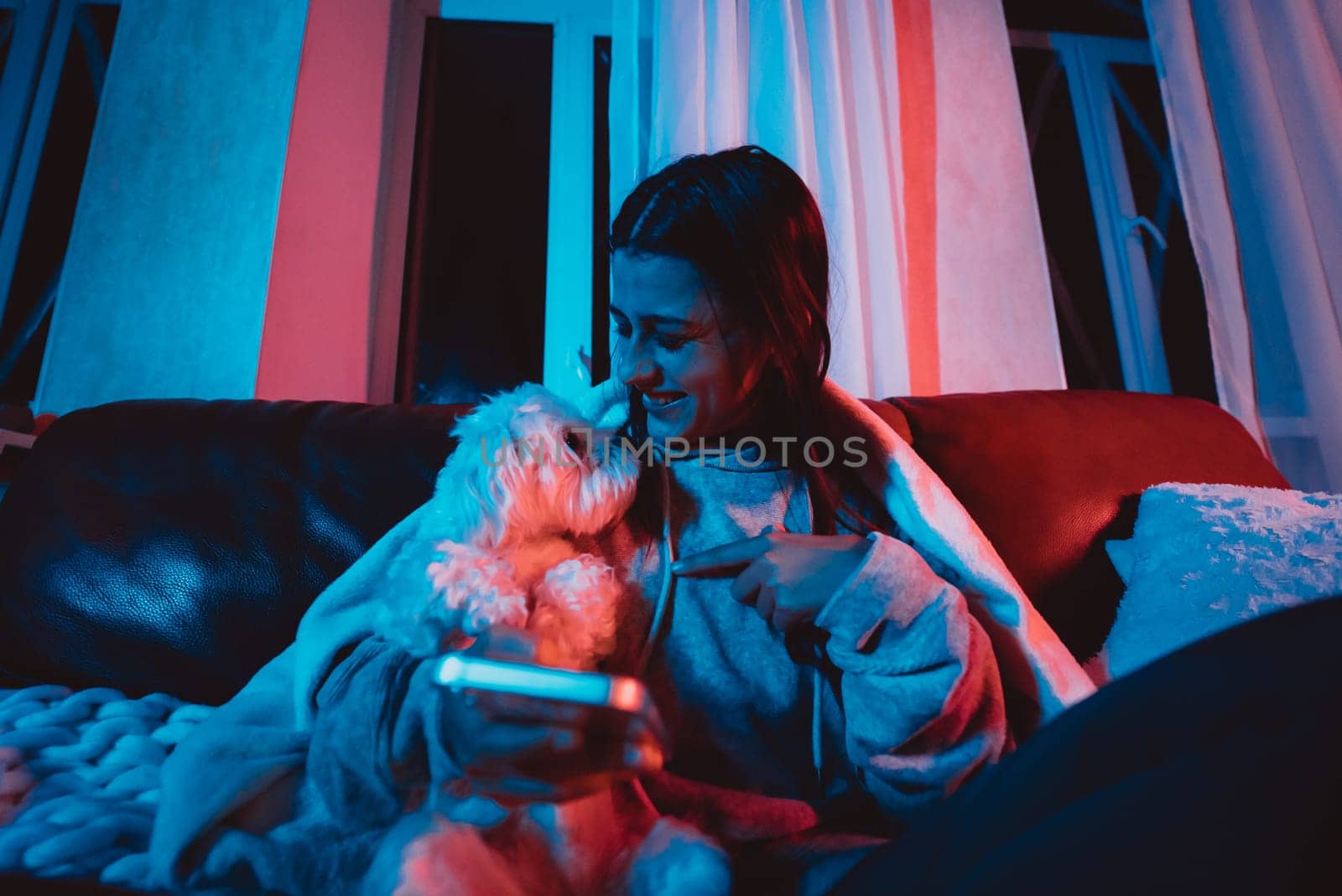 Beautiful young girl at home in a dark room playing with her dog and sits in front of a monitor or TV. High quality photo