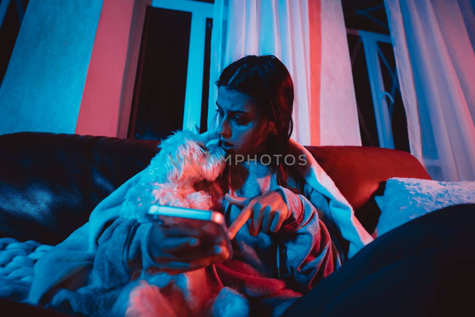 Beautiful young girl at home in a dark room playing with her dog and sits in front of a monitor or TV. High quality photo