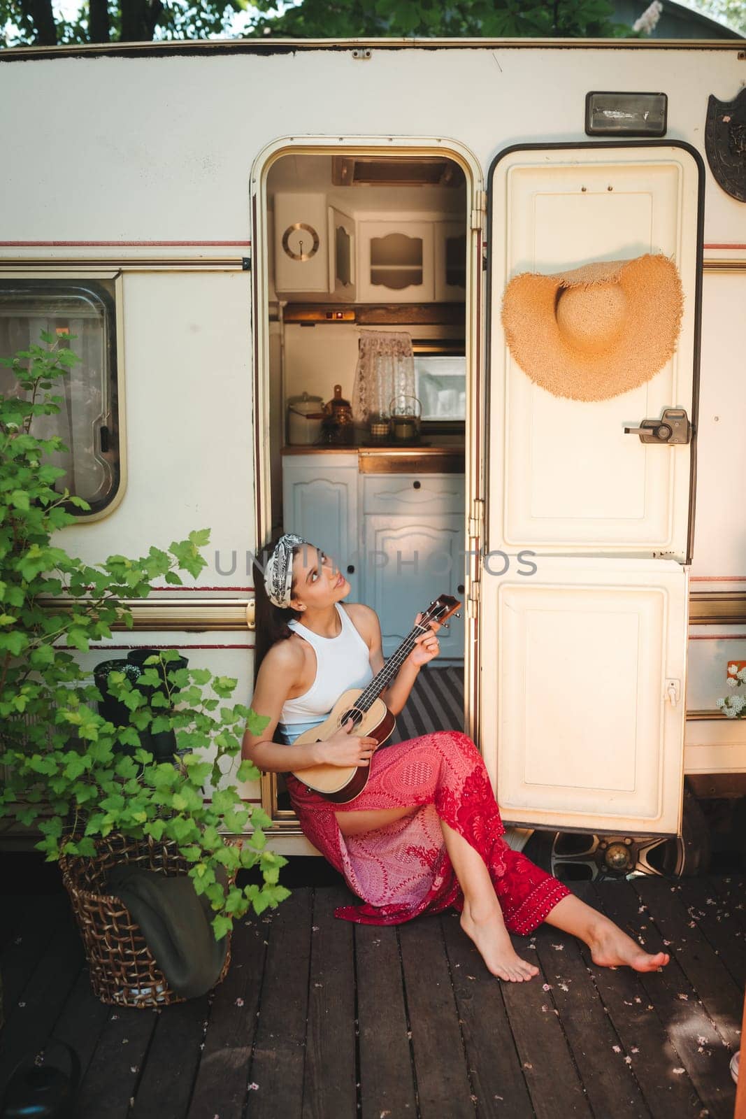 Happy hippie girl are having a good time with playing on guitar in camper trailer. Holiday, vacation, trip concept.High quality photo