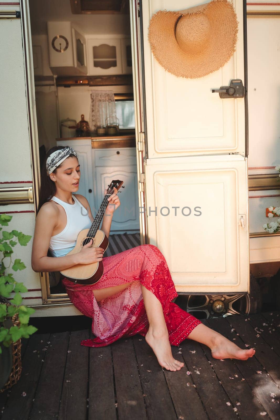 Happy hippie girl are having a good time with playing on guitar in camper trailer. Holiday, vacation, trip concept.High quality photo