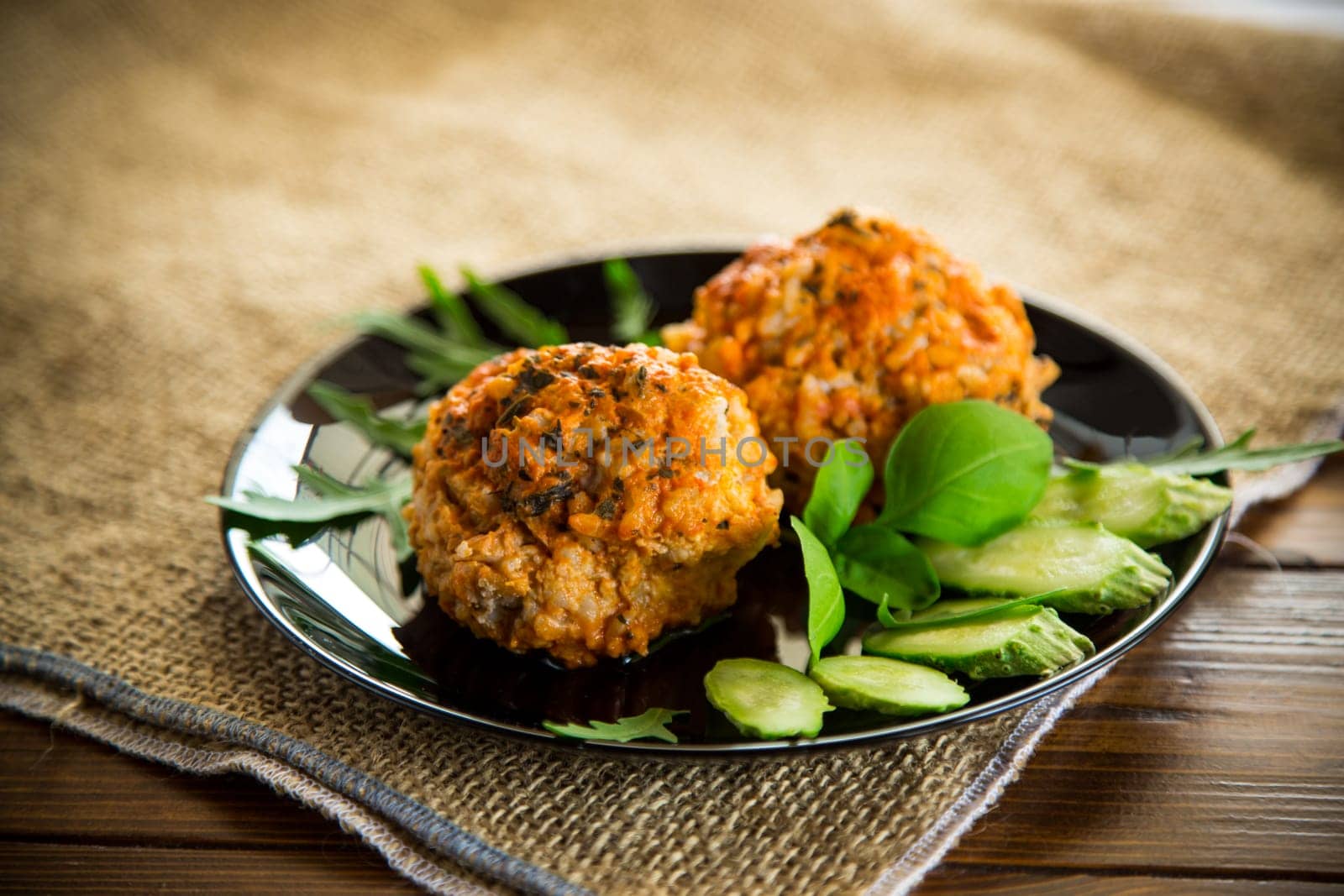 Cooked meatballs in a plate with fresh vegetables, on a wooden table.