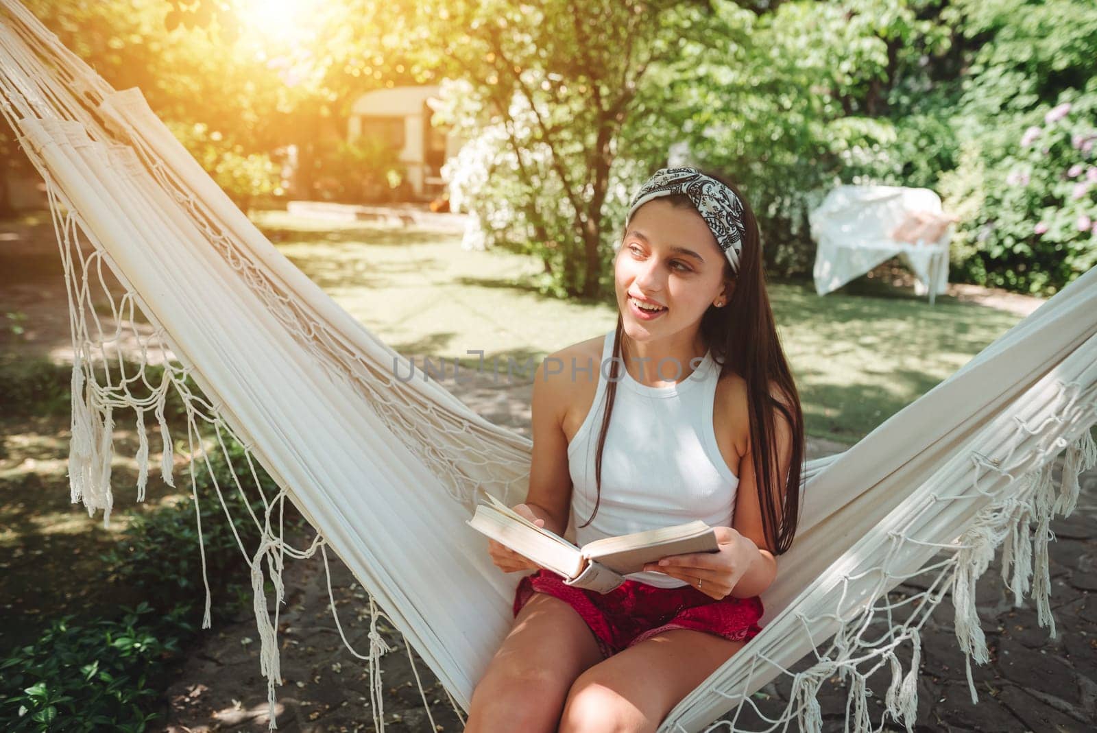 Happy hippie girl is reading a book in hammock having a good time with playing in camper trailer. Holiday, vacation, trip concept.High quality photo