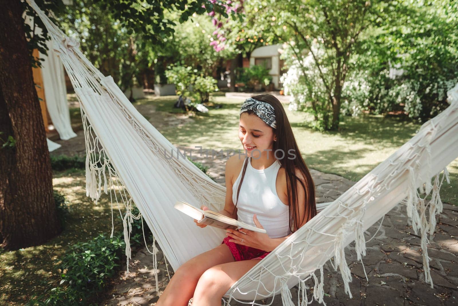 Happy hippie girl is reading a book in hammock having a good time with playing in camper trailer. Holiday, vacation, trip concept.High quality photo