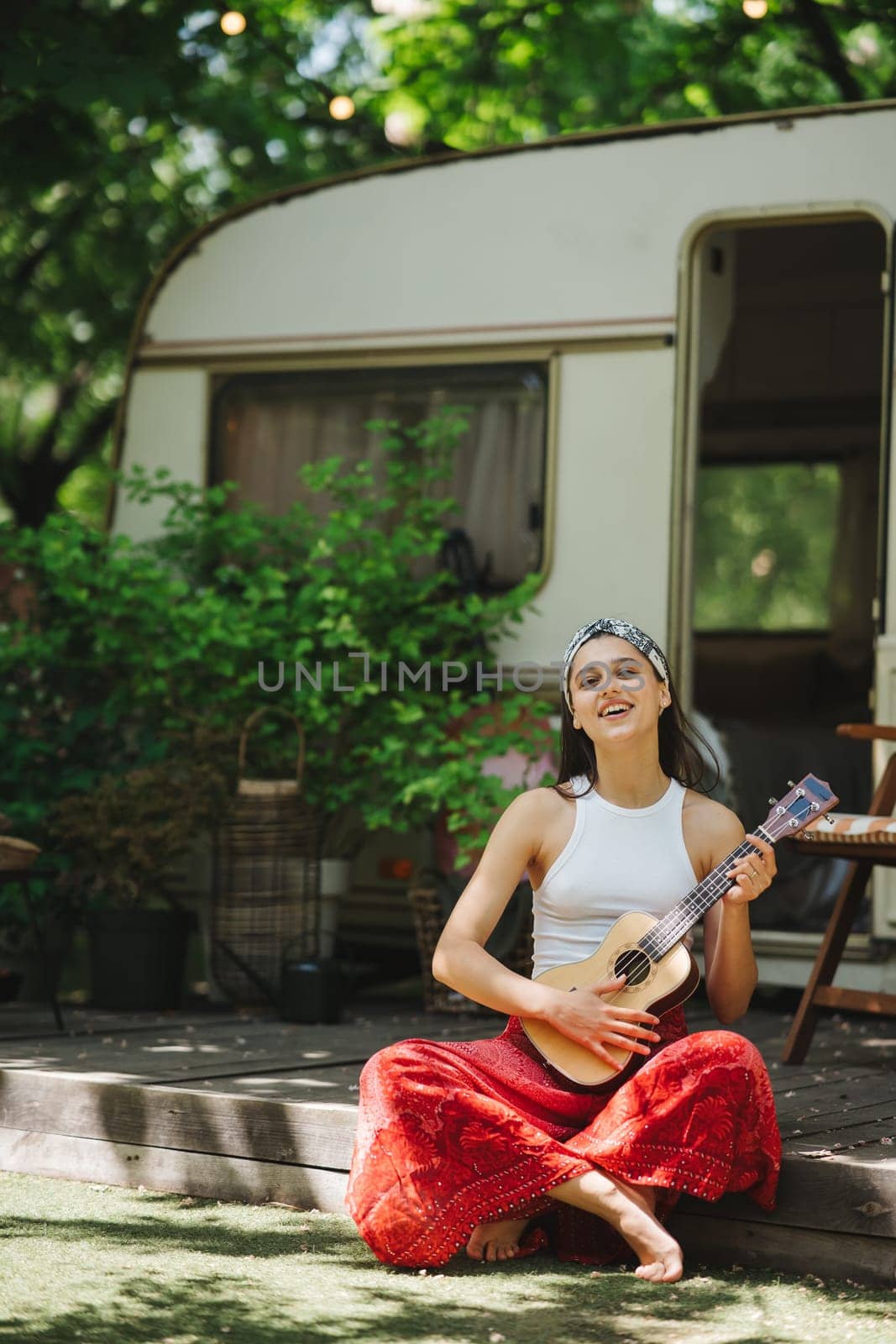 Happy hippie girl are having a good time with playing on guitar in camper trailer. Holiday, vacation, trip concept.High quality photo