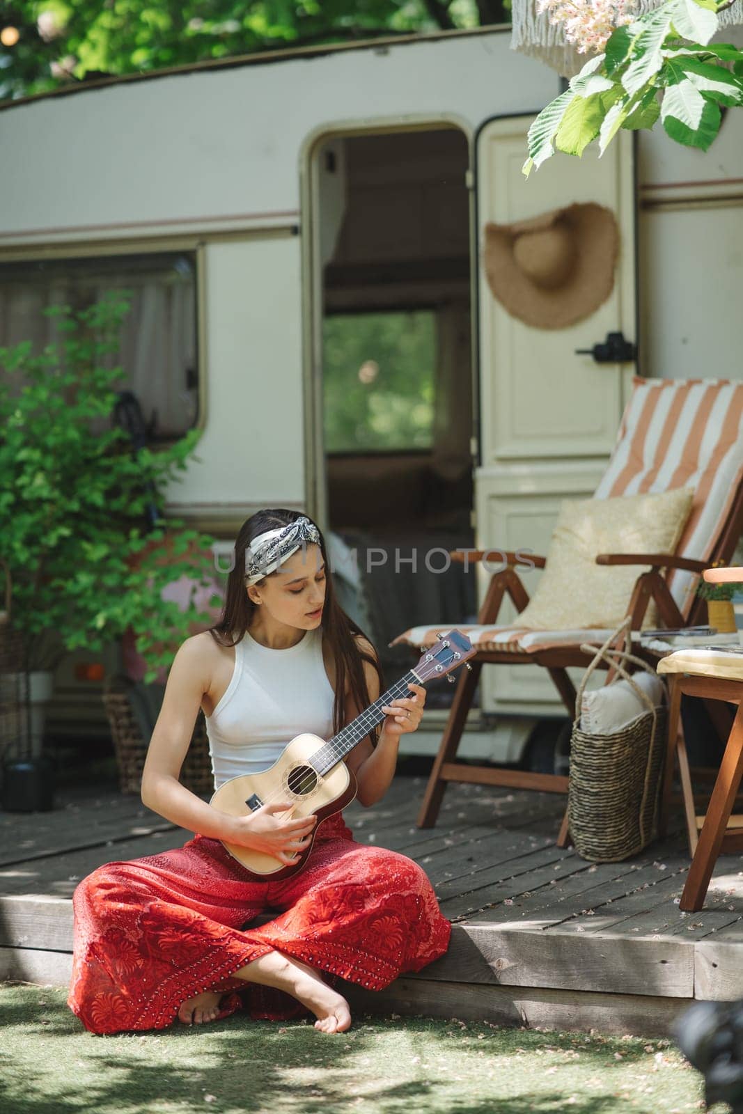 Happy hippie girl are having a good time with playing on guitar in camper trailer. Holiday, vacation, trip concept.High quality photo