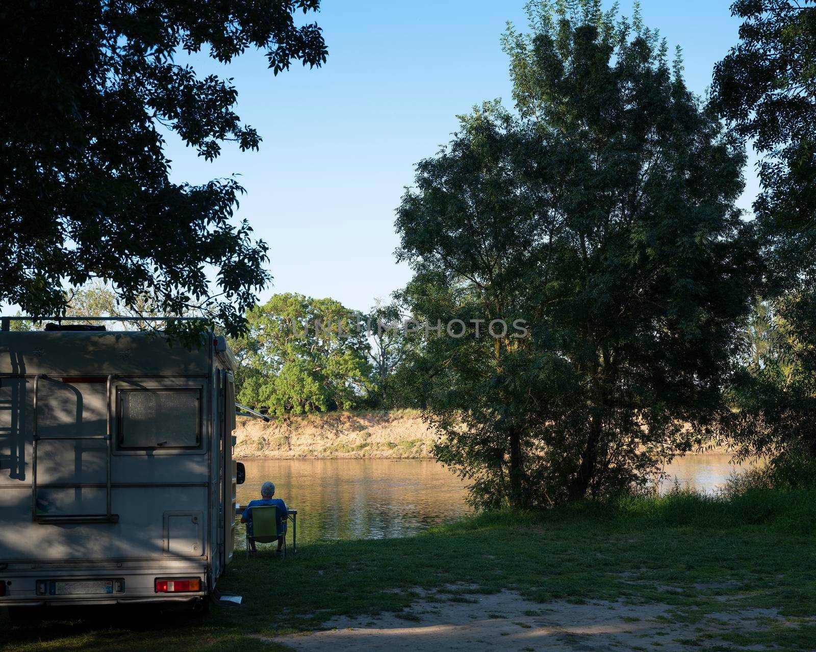 man sits next to camper on embankment of river loire in france by ahavelaar