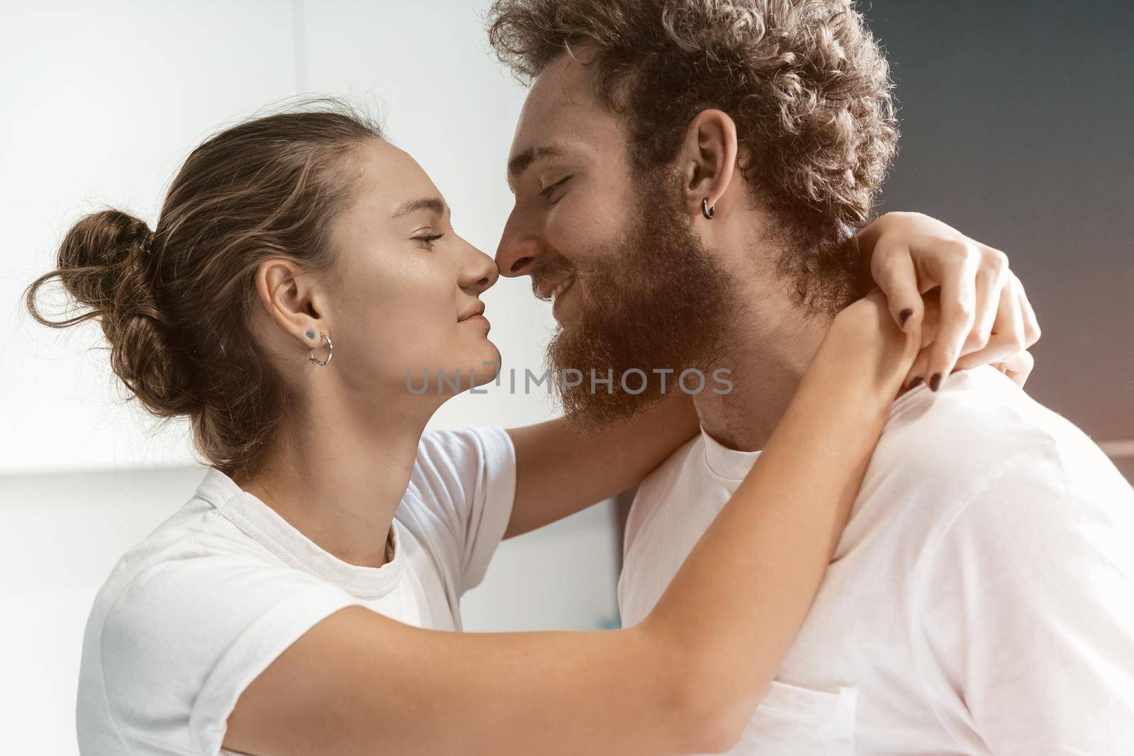 Romantic couple in love. Close up portrait. Young man kissing his wife standing at the kitchen. Morning kiss to a wife, young couple flirting in the kitchen. Intimate moment between a couple.