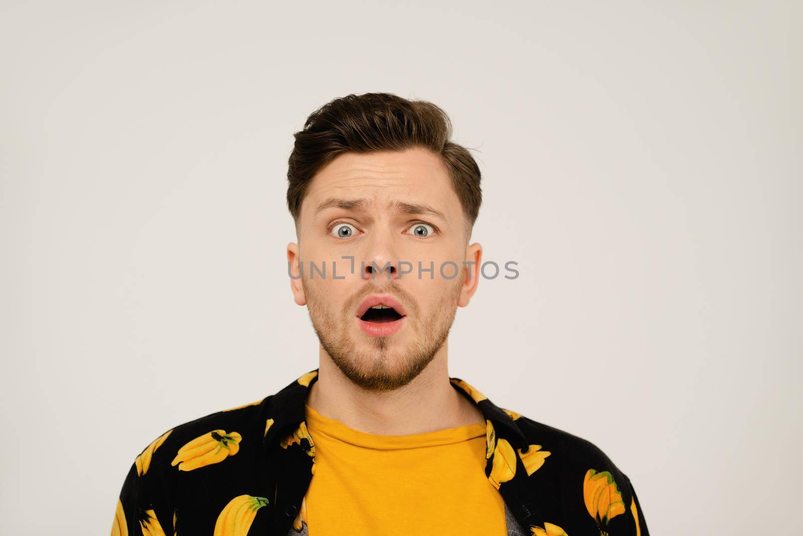 Surprised or shocked look on face of handsome man in dressed banana shirt and yellow t-shirt under looking at camera. Isolated on white background. Close up shot.