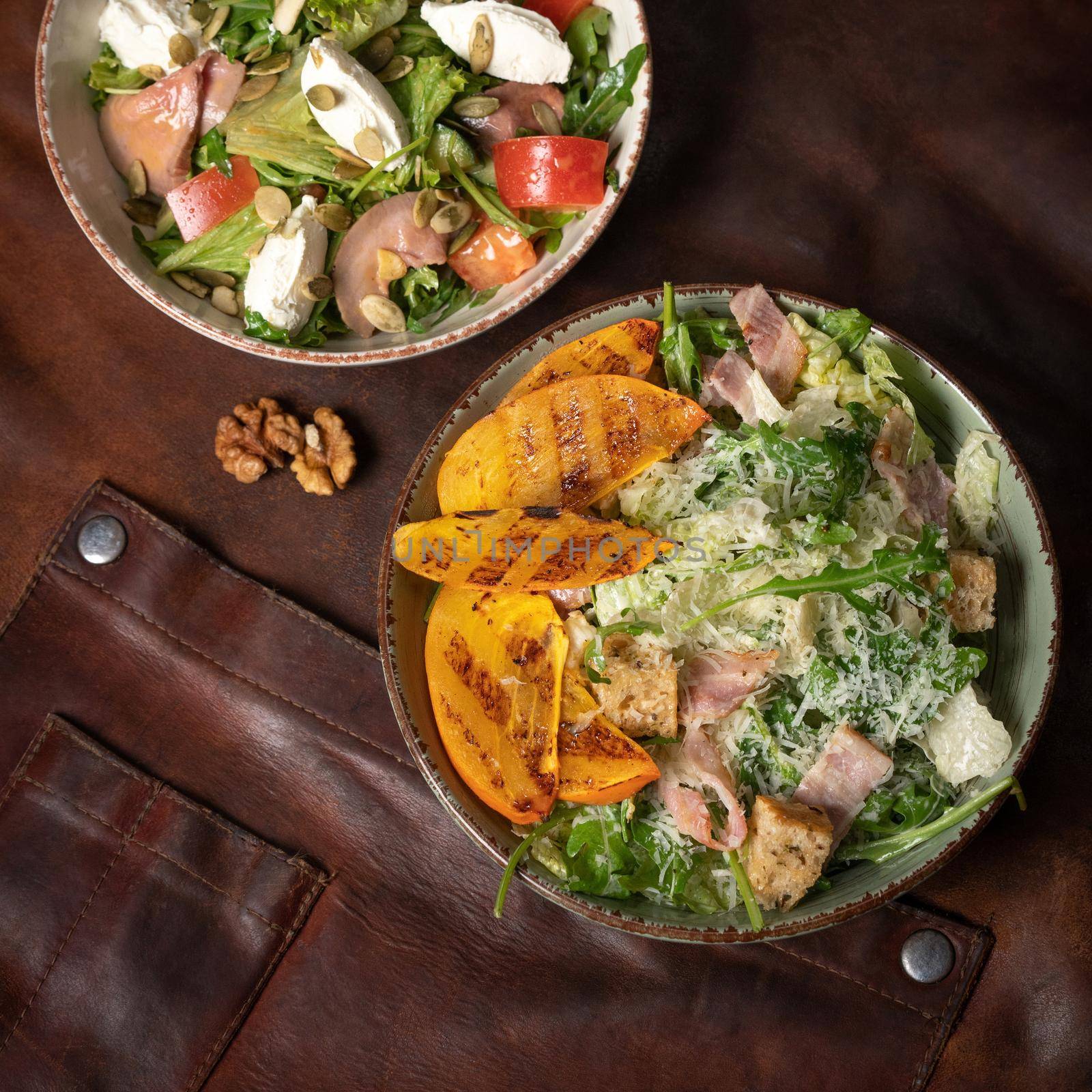 Salmon salads with mozzarella cheese and grilled slices of fruits stands on a table covered with a leather rag. Restaurant concept. Square cropped image. KETO diet concept. Whole30 concept by LipikStockMedia