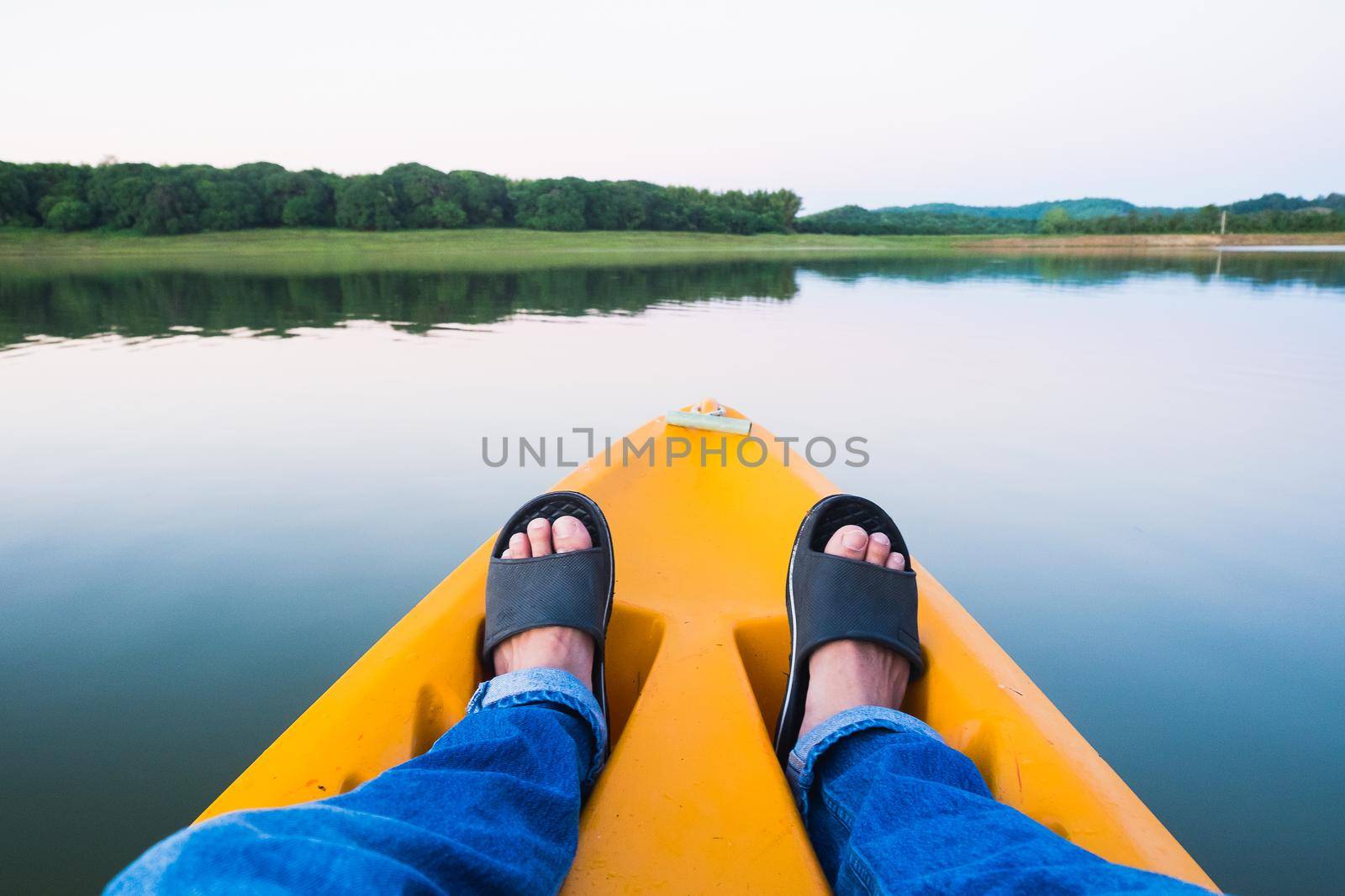 Feet relaxing on orange kayak floating on river and autumn