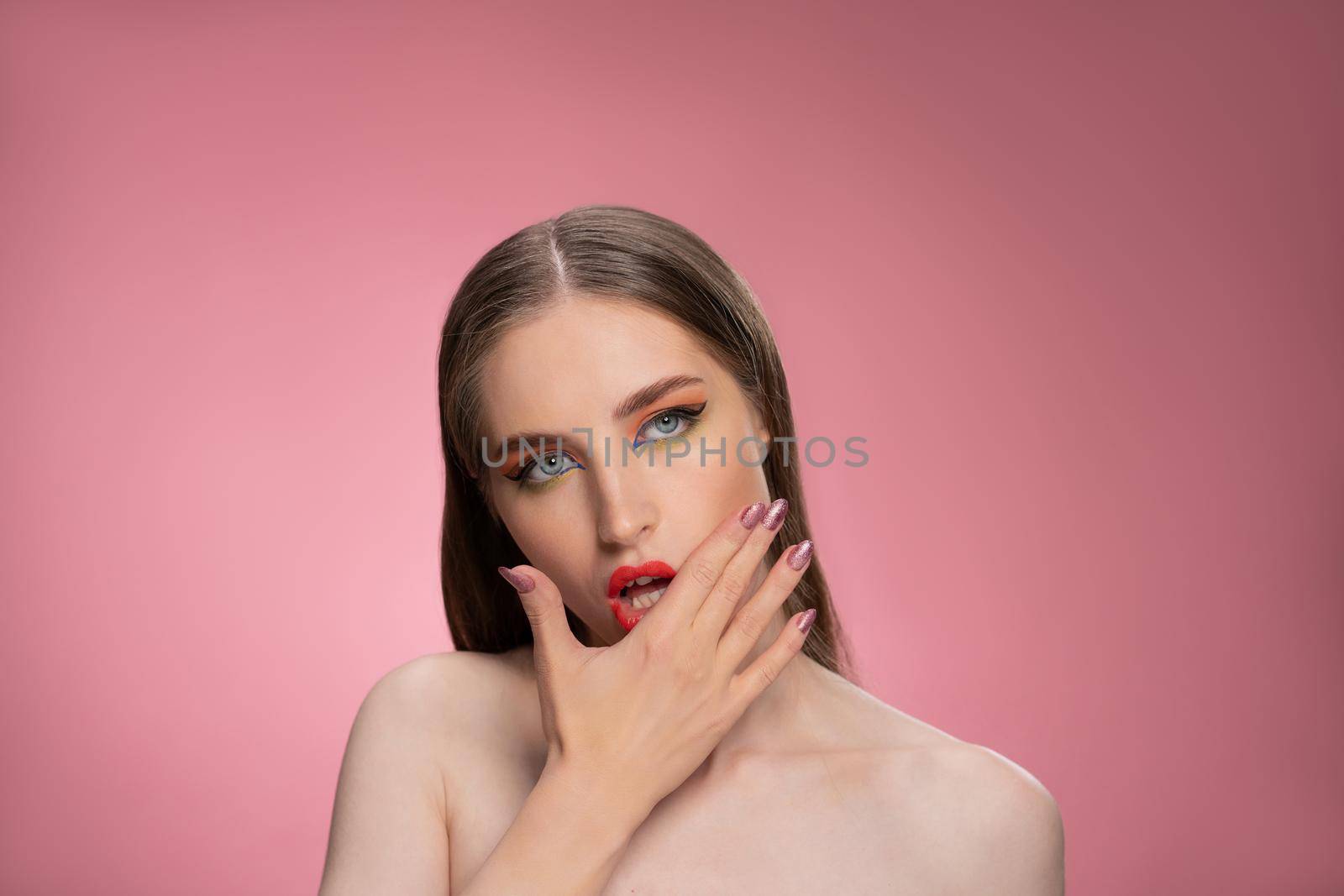 Messing up lipstick on face fashion model beautiful woman with long straight hair standing in the studio isolated on dirty pink background. Lips make up concept. 