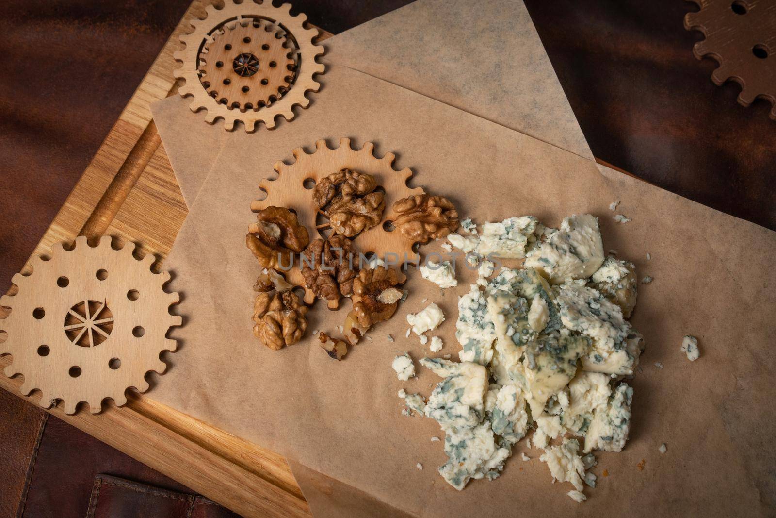 Top view of a blue cheese or bleu cheese served with walnuts on food wrapping paper and chalkboard with decorative wooden details of a simple mechanism. Cheese with the mold. 