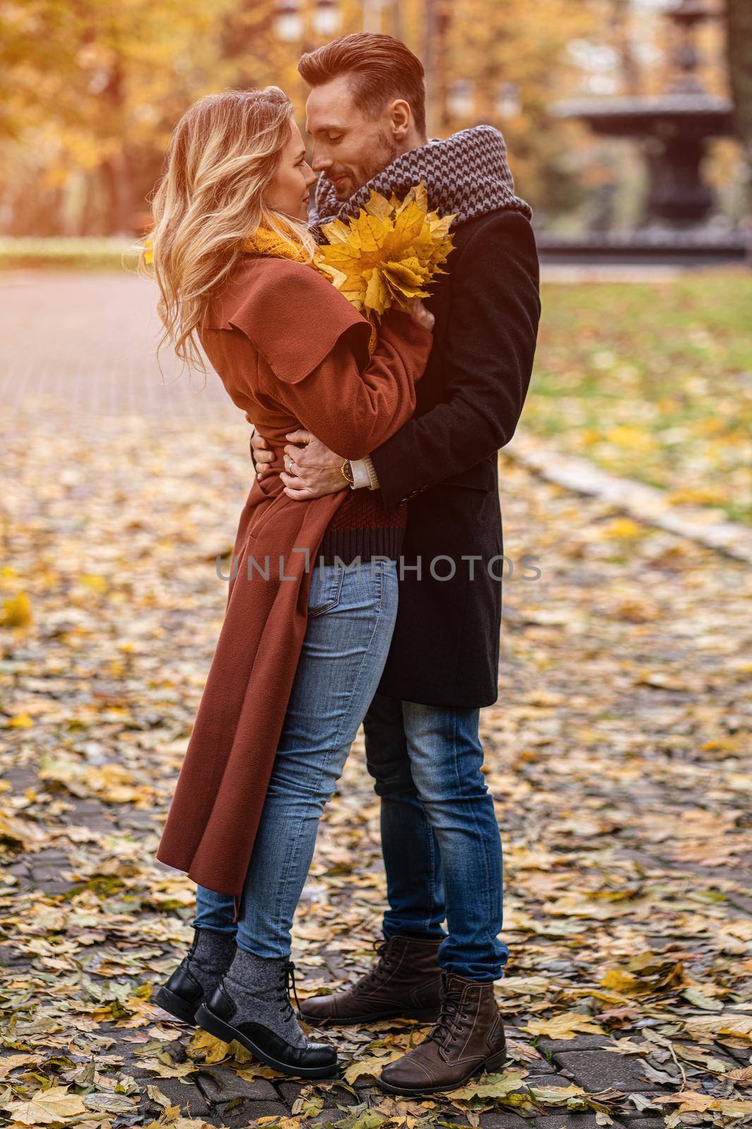 Kissing young couple. Husband and a wife hugged smile looking at each other in the autumn park. Outdoor shot of a young couple in love having great time in a autumn park.